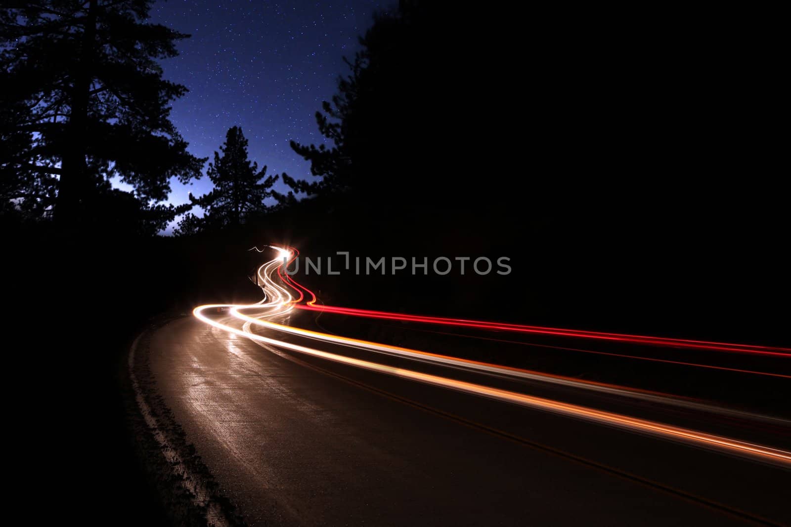 Car Light Trails in the Mountains on a Starry Night Alongside the Highway. Noise is Present in the Sky Due to Shooting Conditions.