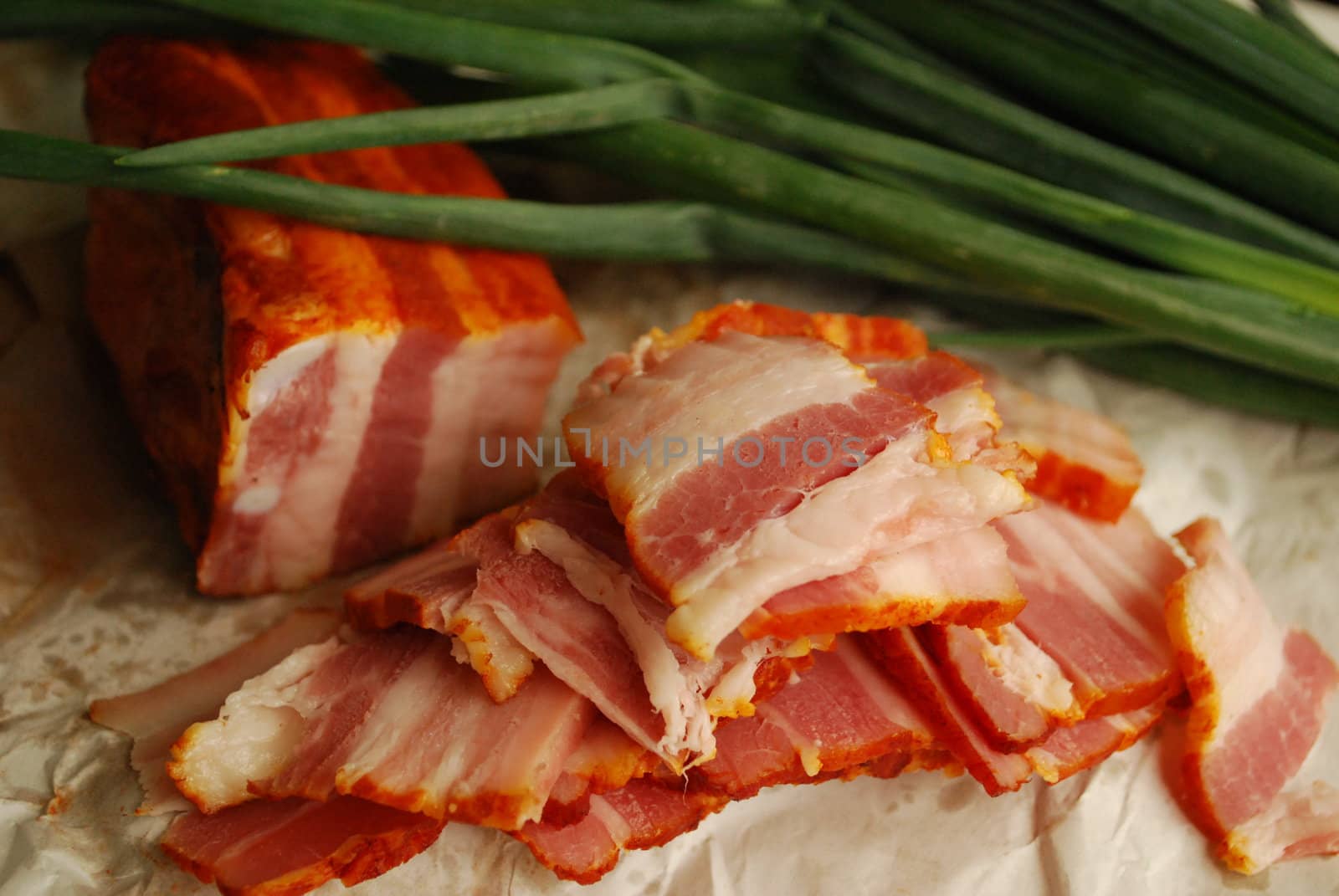 Bacon slices near a green onion on a paper
