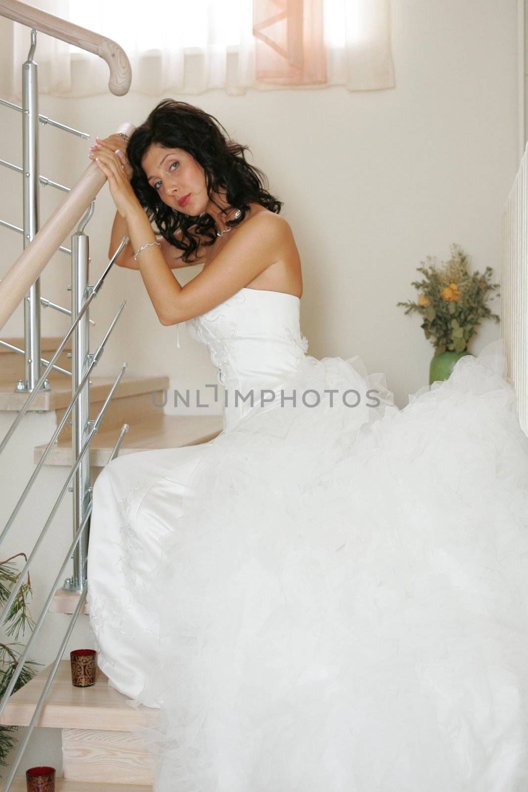 Close up of beautiful young bride wearing long white dress and sat on stairs.