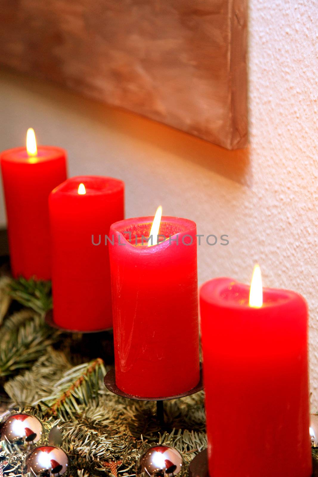 Four red Christmas candles are burning. In the foreground are silver-colored Christmas tree ball to see close-up-
