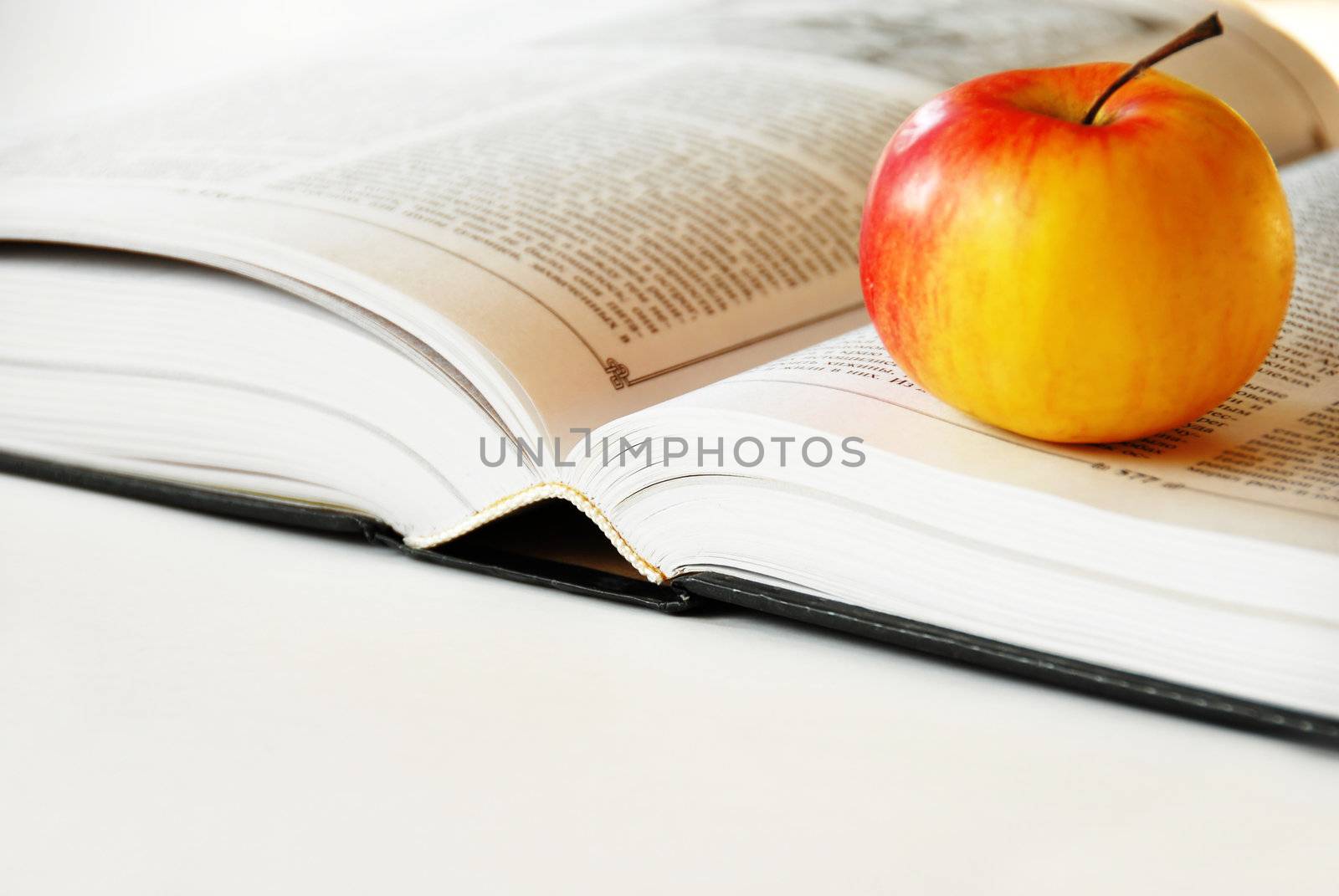 large opened book with ripe red yellow apple