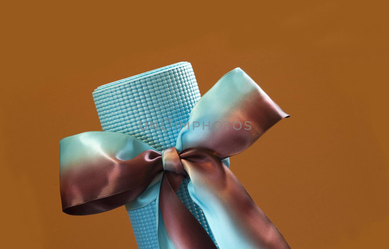 Blue yoga mat placed at an angle and tied like a gift with blue and tan satin ribbon against a tan wall that provides copy space