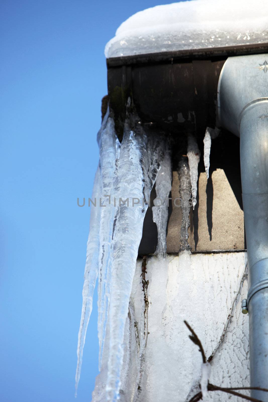 dangerous, large icicles hanging from the gutter in front of blue sky
