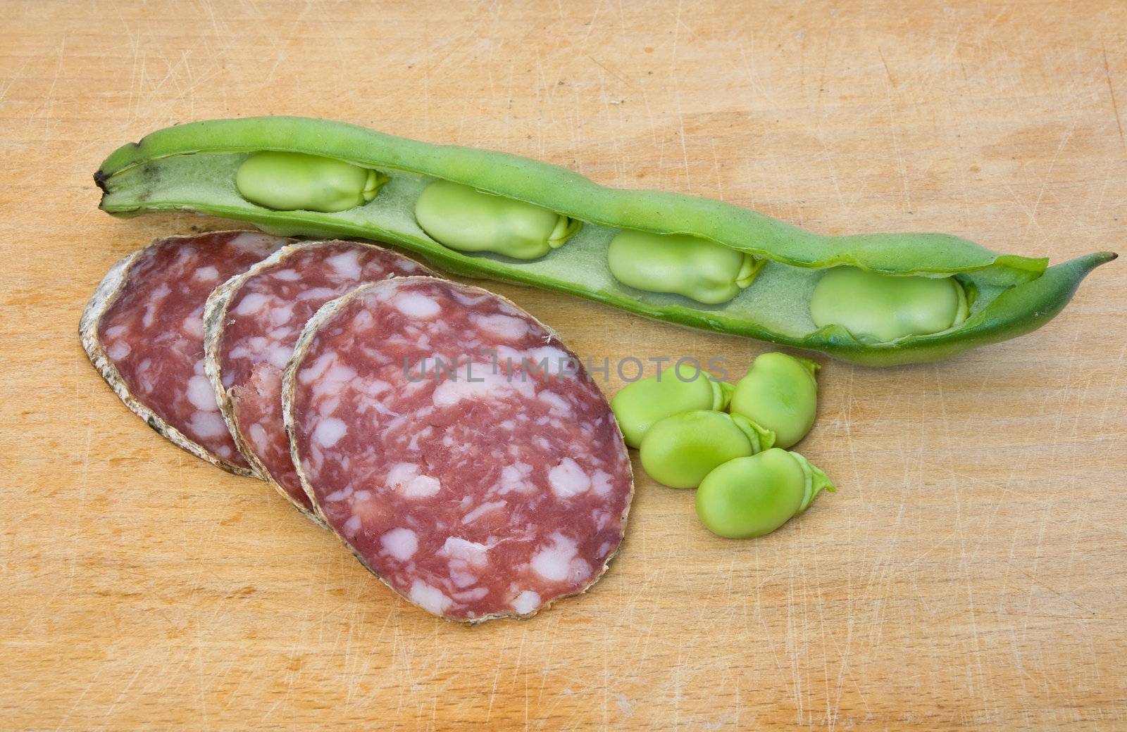 Three salami slices with broad beans on a wood chopping board