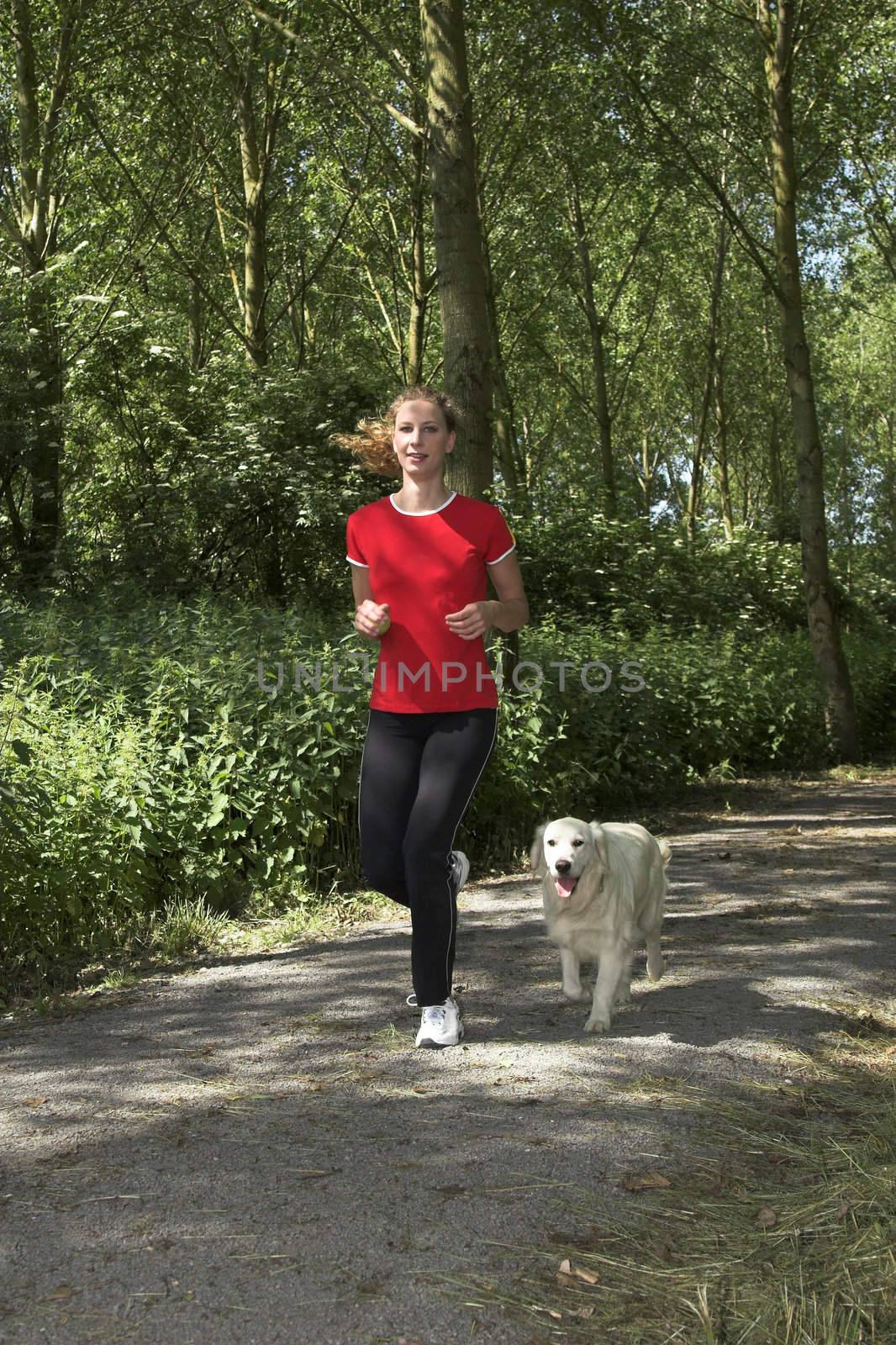 Pretty blond woman running in the woods with her dog