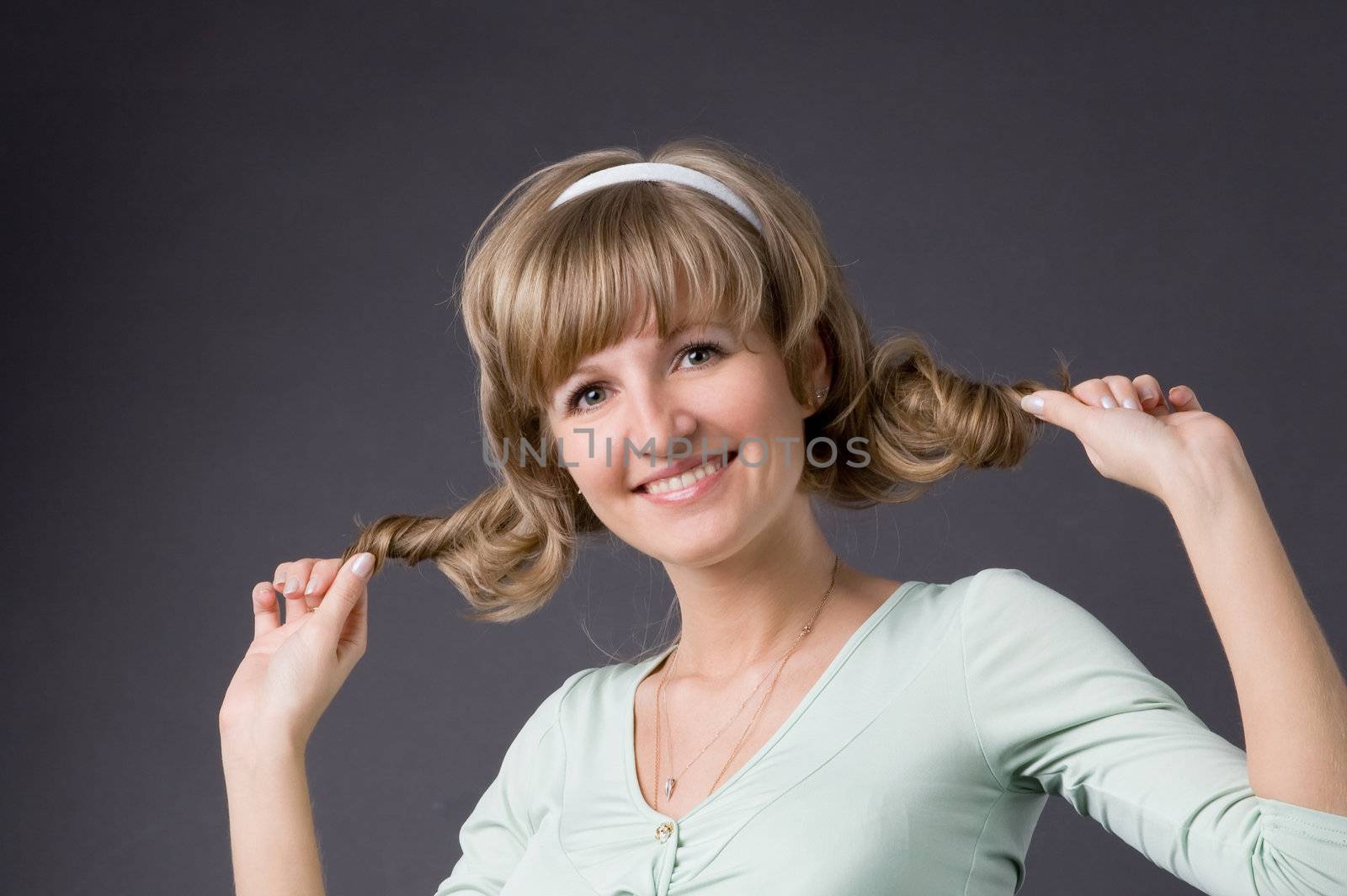 The girl tightens up hair in studio on a grey background