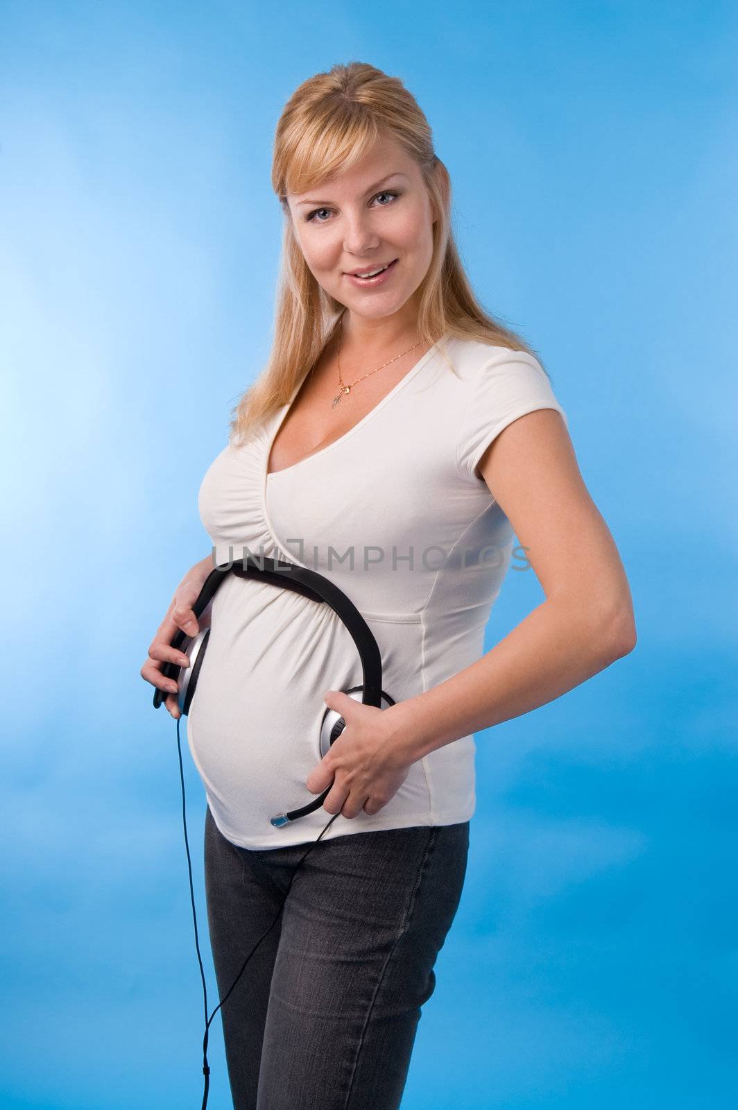 The beautiful pregnant woman with headphones on a stomach.