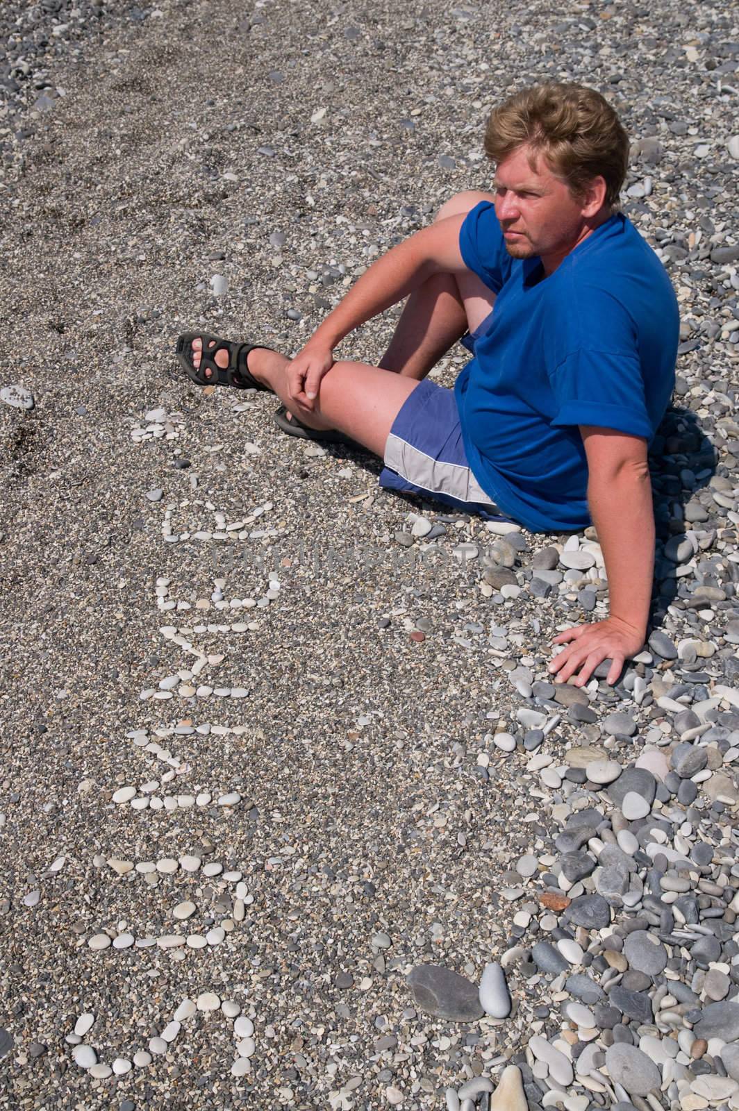 Sunburnt man sits on a stone beach, near to an inscription "summer".