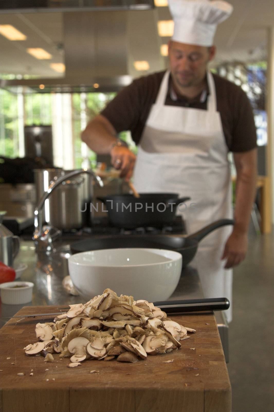 Italian chef stirring the food on the stove (focus is on the mushrooms in the front)