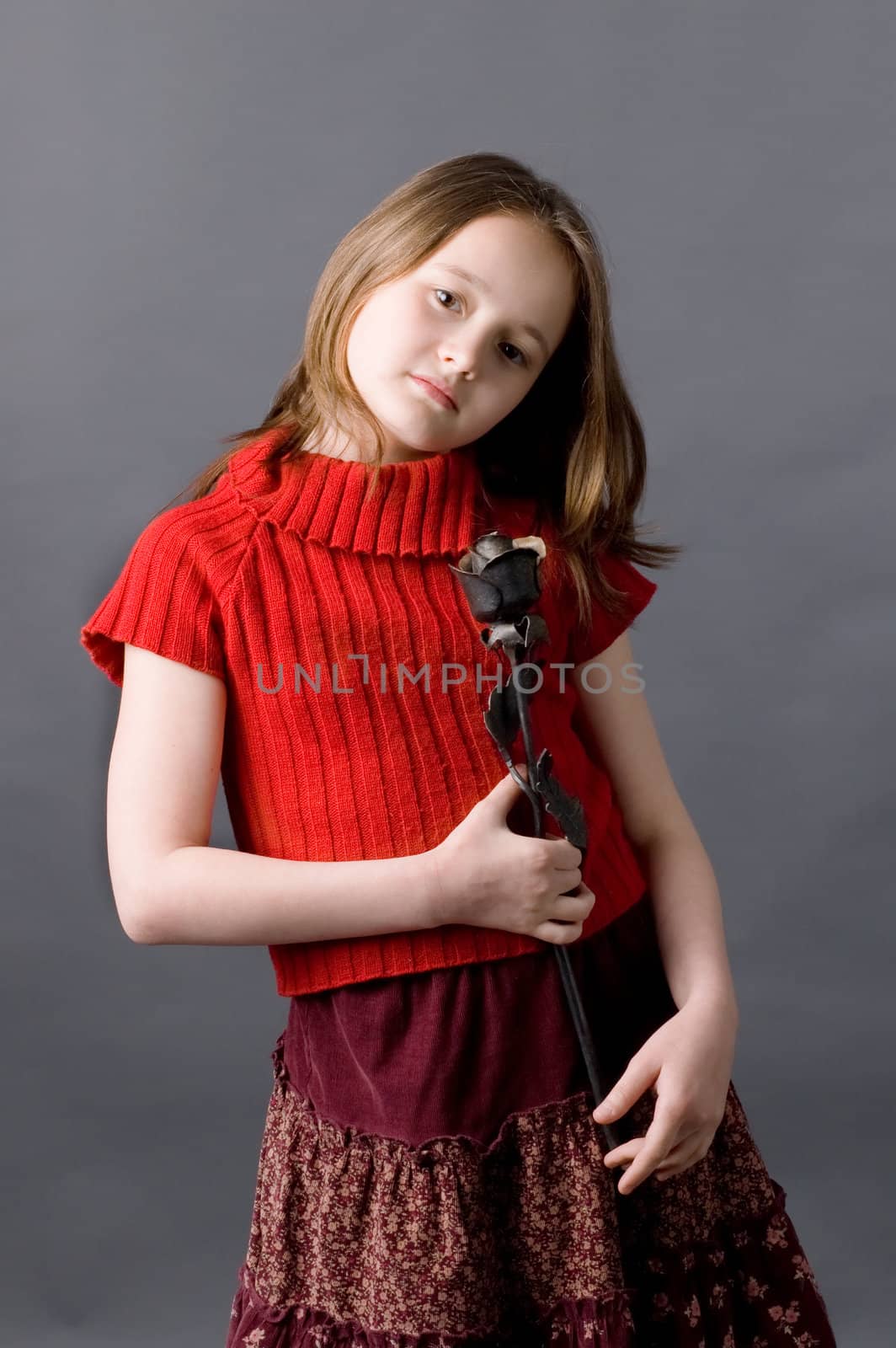 The girl of ten years with an iron rose in hands on a grey background
