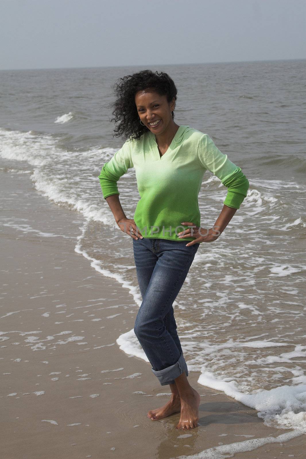 Beautiful black woman having fun on the beach standing by the waterline