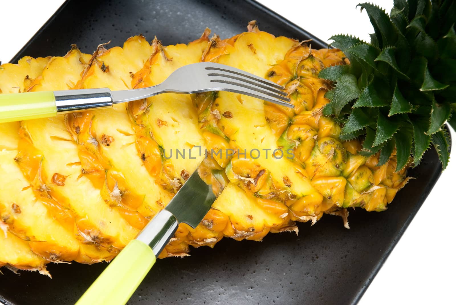 ripe vibrant pineapple sliced on a black plate with knife and fork