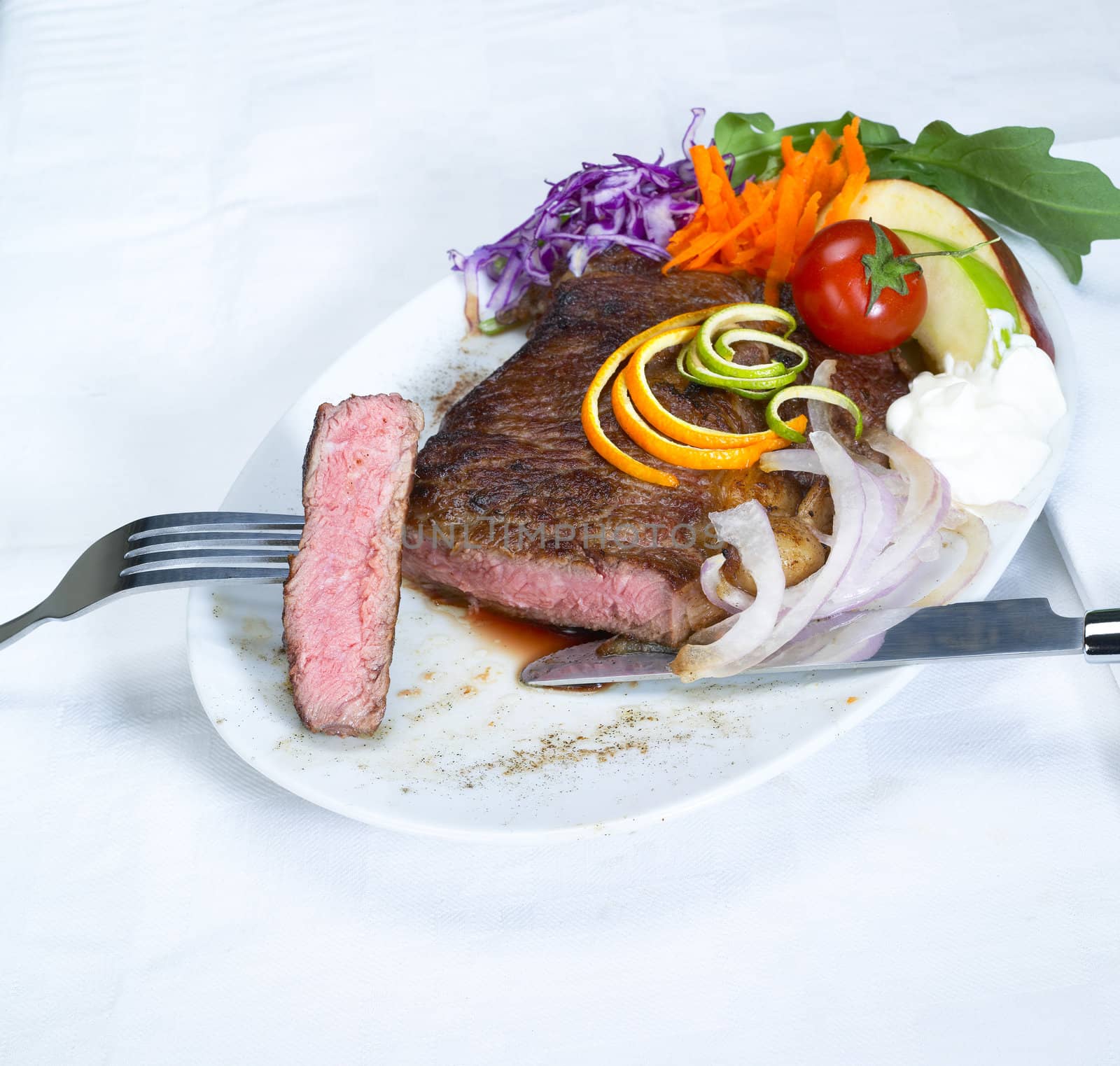 fresh juicy beef ribeye steak grilled with lemon and orange peel on top and vegetables beside with sour cream