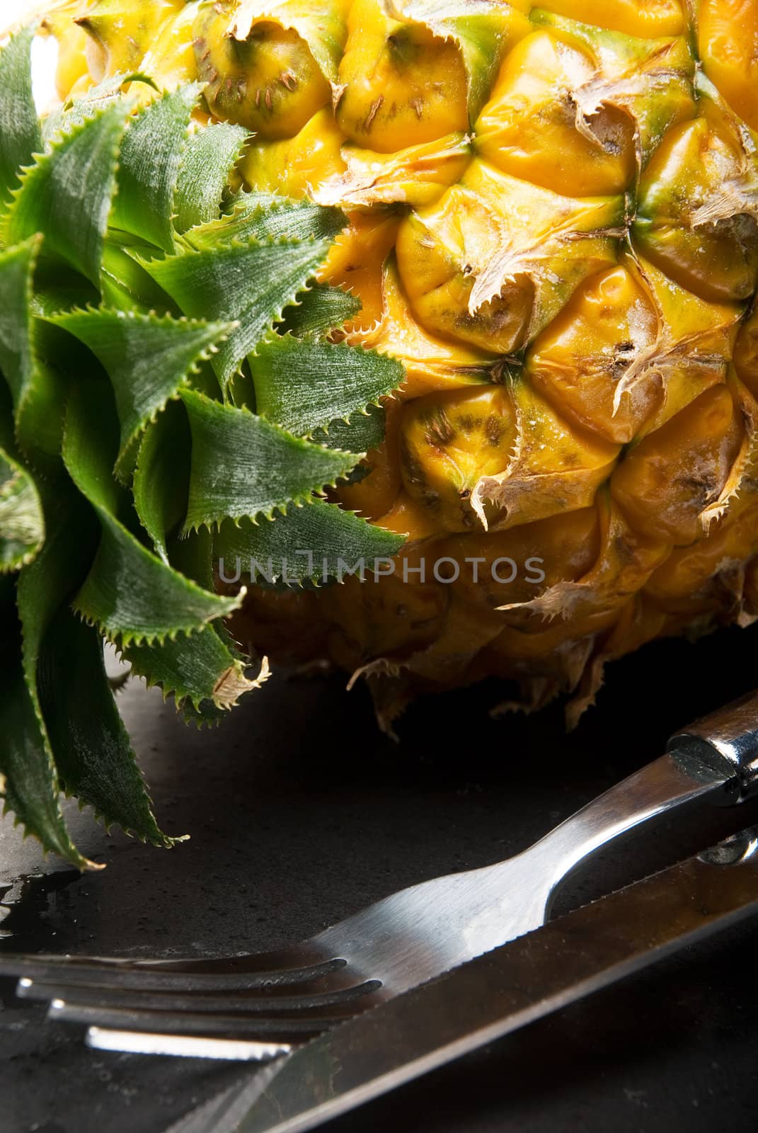 ripe pineapple on a black plate with knife and fork