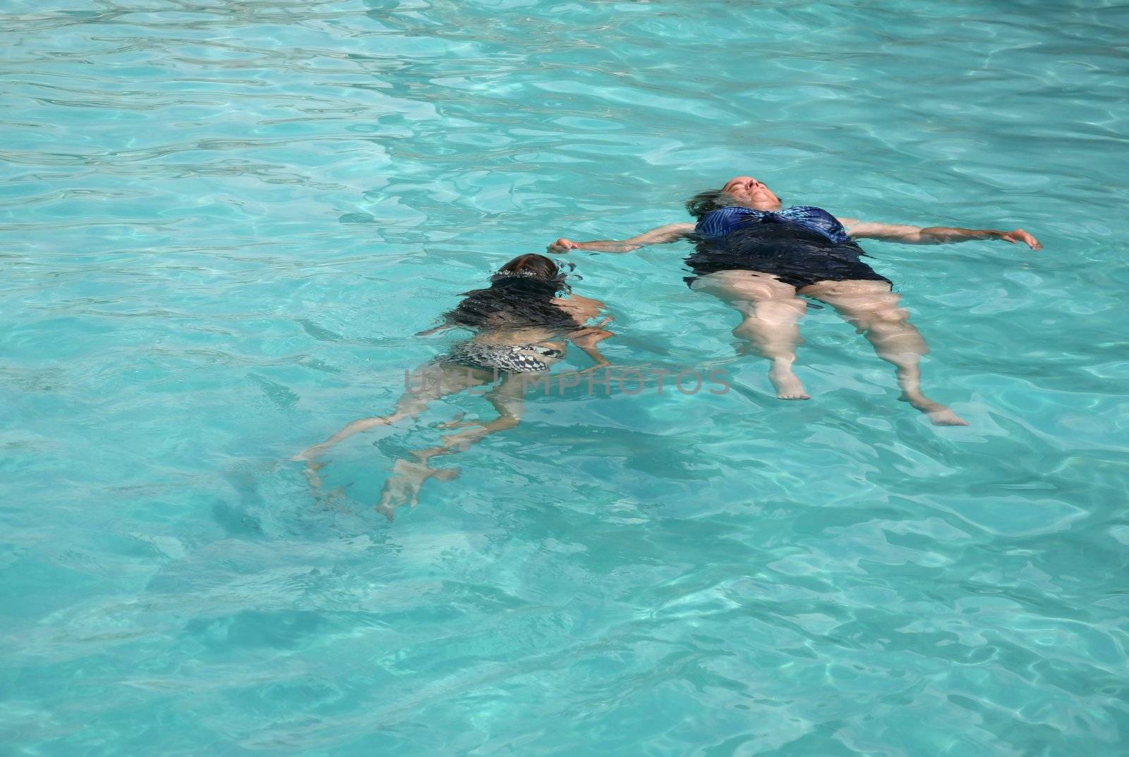 Young girl watching her mother float in a swimming pool