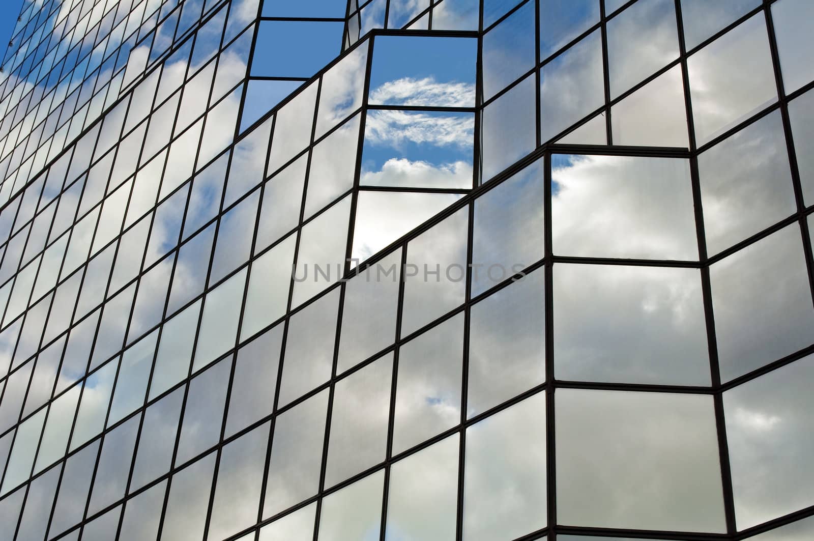 Modern glass office building with clouds and sky reflections.