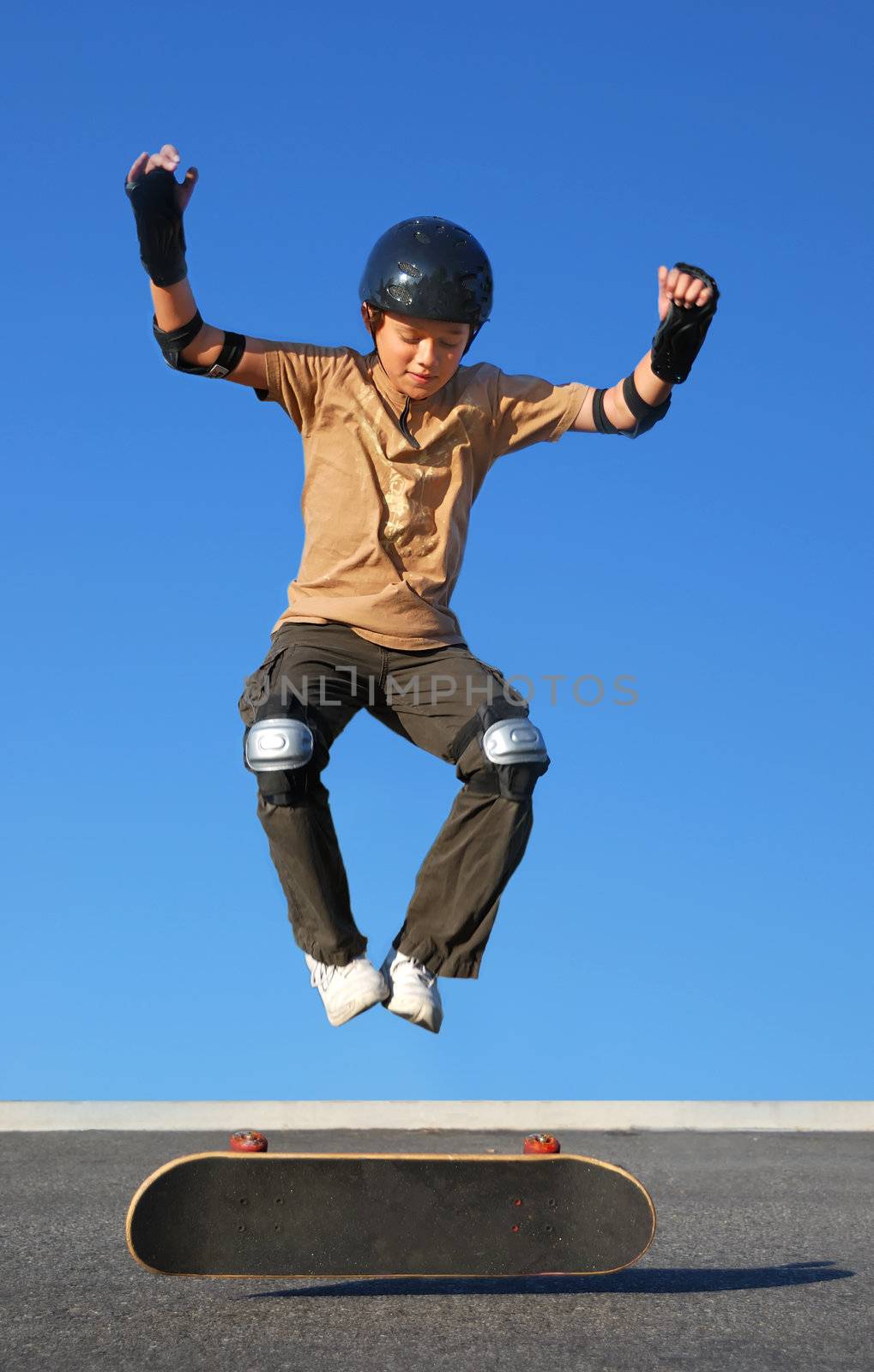 Boy with protective gear jumping high from a skateboard with blue background.