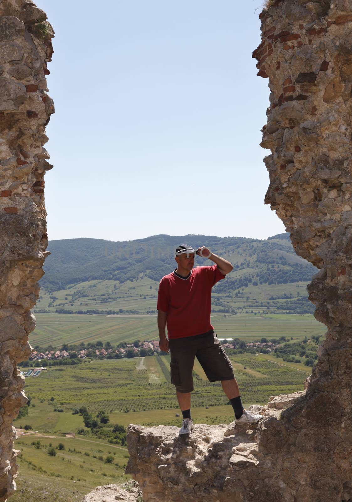 Man scrutinizing the horizon from a rocky fortress ruin in a mountainous area.