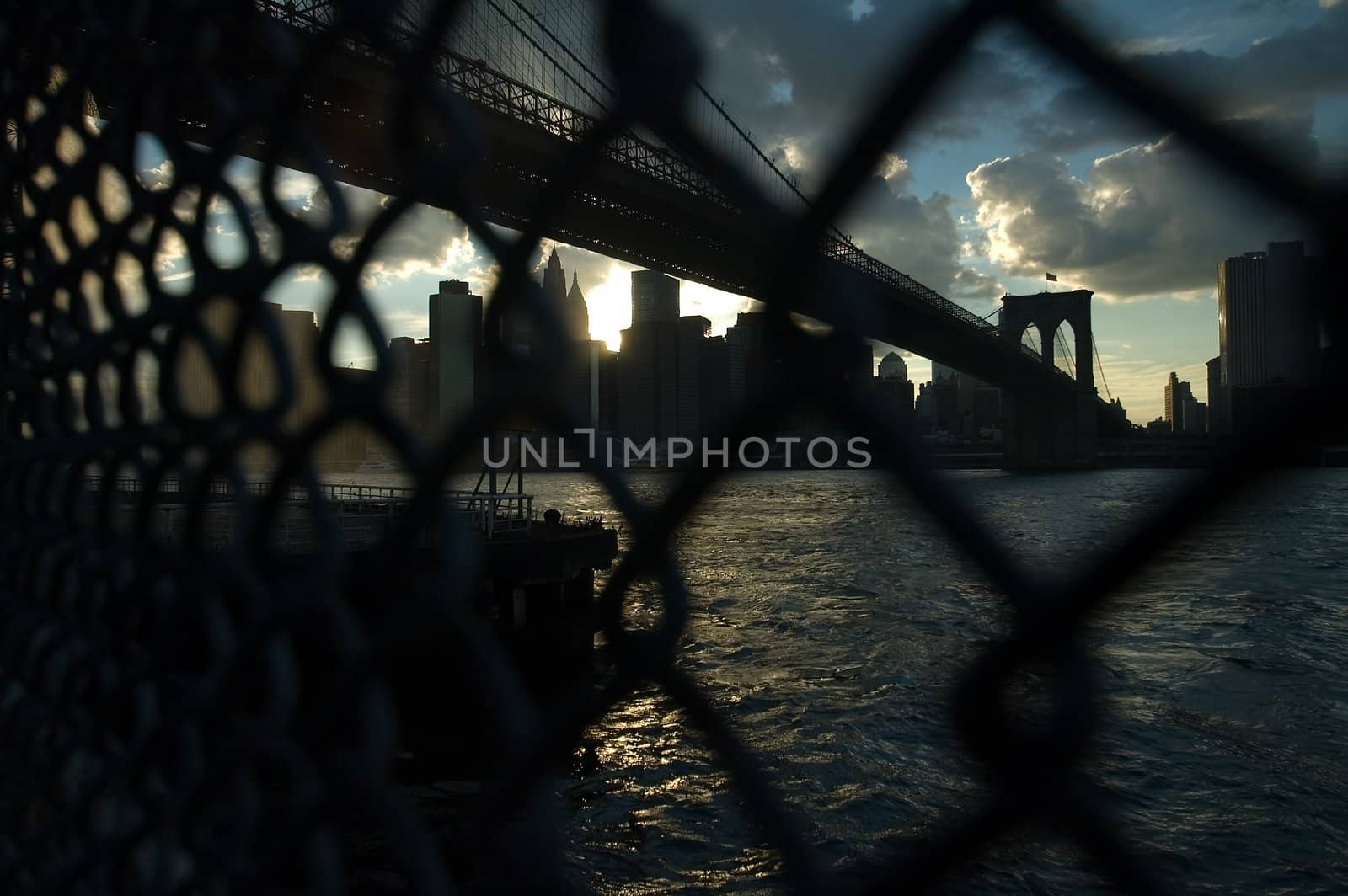 dark photo of brooklyn bridge behind a fence, silhouettes of lower manhattan