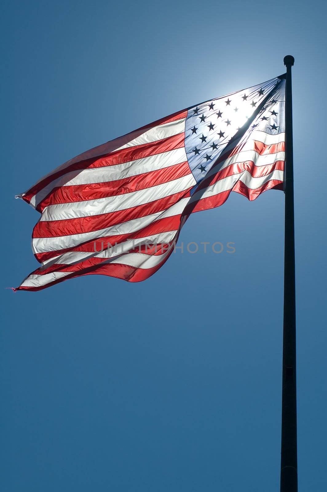 waving american flag, clear blue sky, sun is directly behind the flag