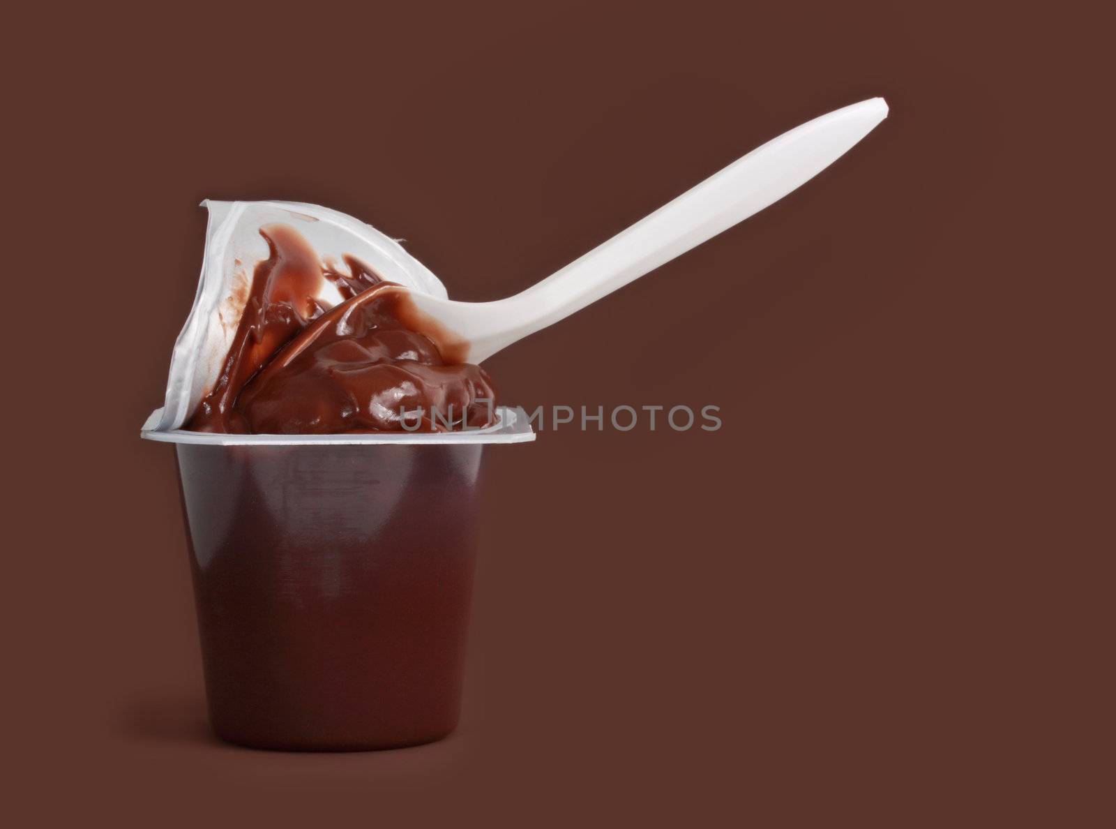 chocolate pudding and plastic spoon, brown background