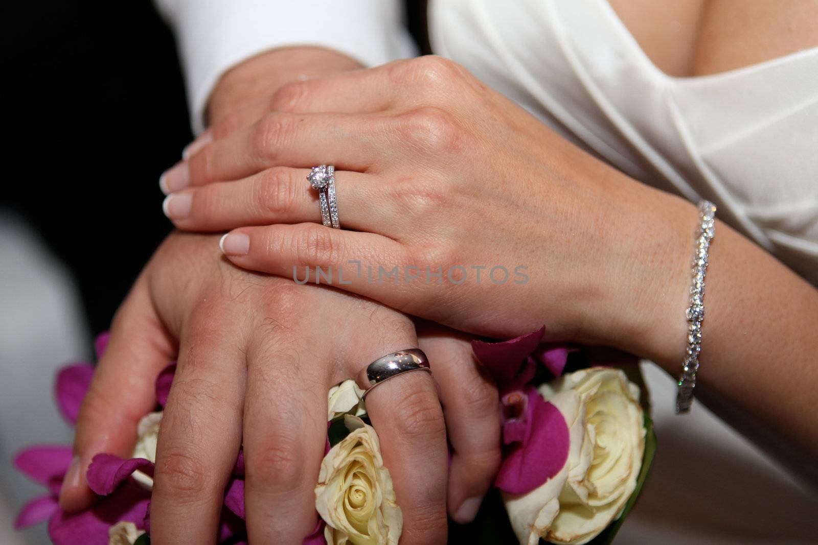 Close-up of a bride and groom's hands at the beach during a wedding ceremony.