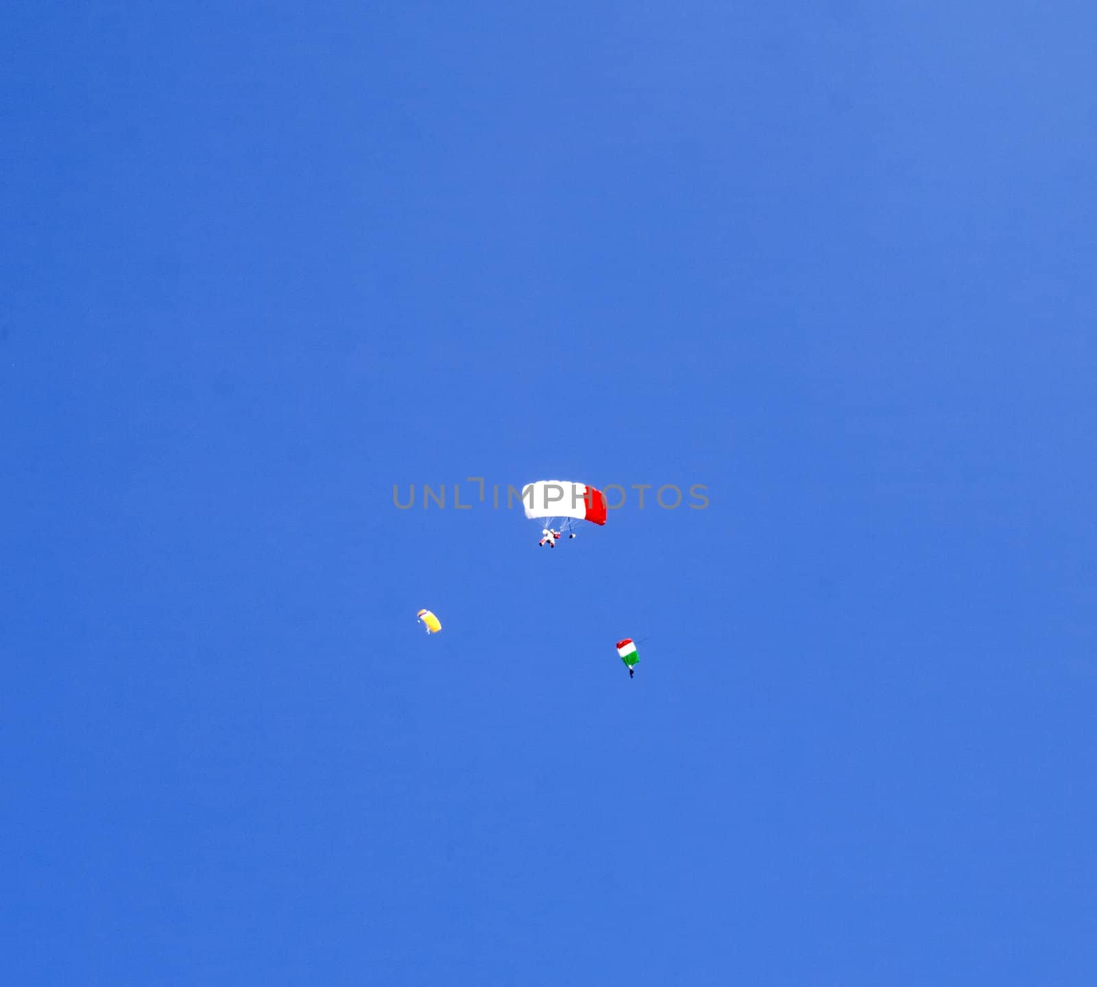 Three parachutists fly in deep blue sky