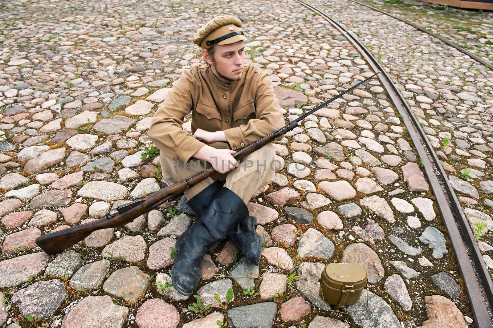 Soldier with gun and boiler in uniform of World War I, sit down and resting on the pavement. Costume accord the times of World War I. Photo made at cinema city Cinevilla in Latvia.