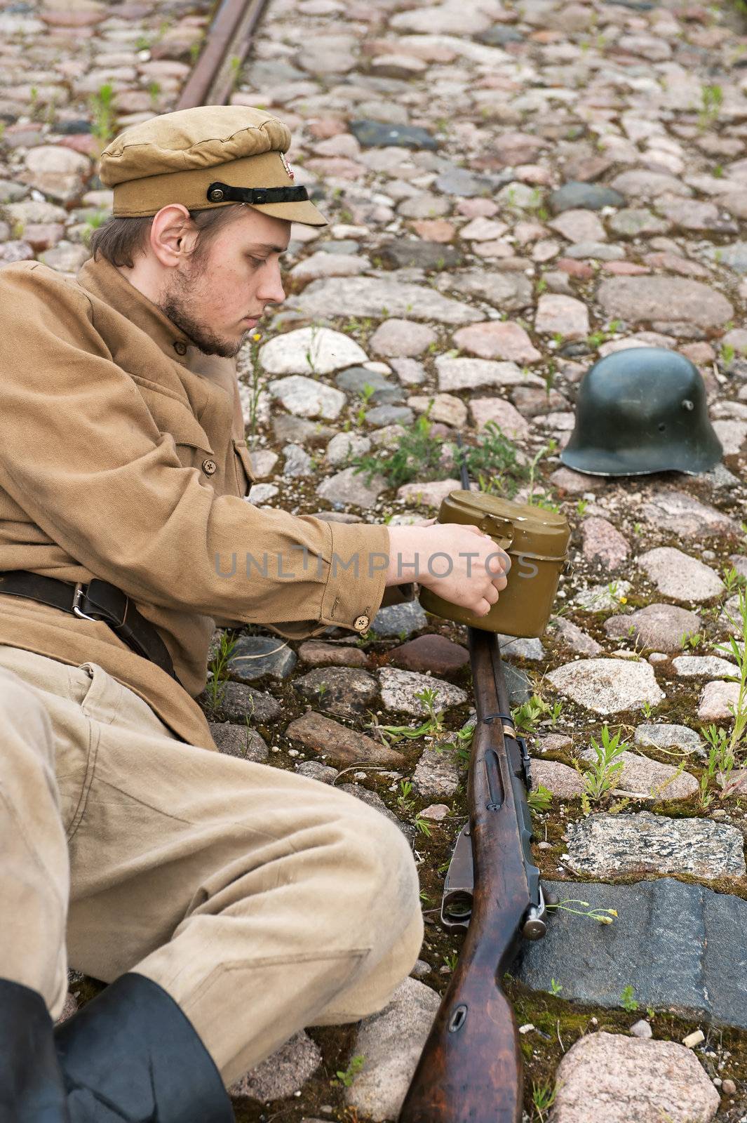 Soldier with gun and boiler in uniform of World War I, resting on the pavement. Costume accord the times of World War I. Photo made at cinema city Cinevilla in Latvia. 