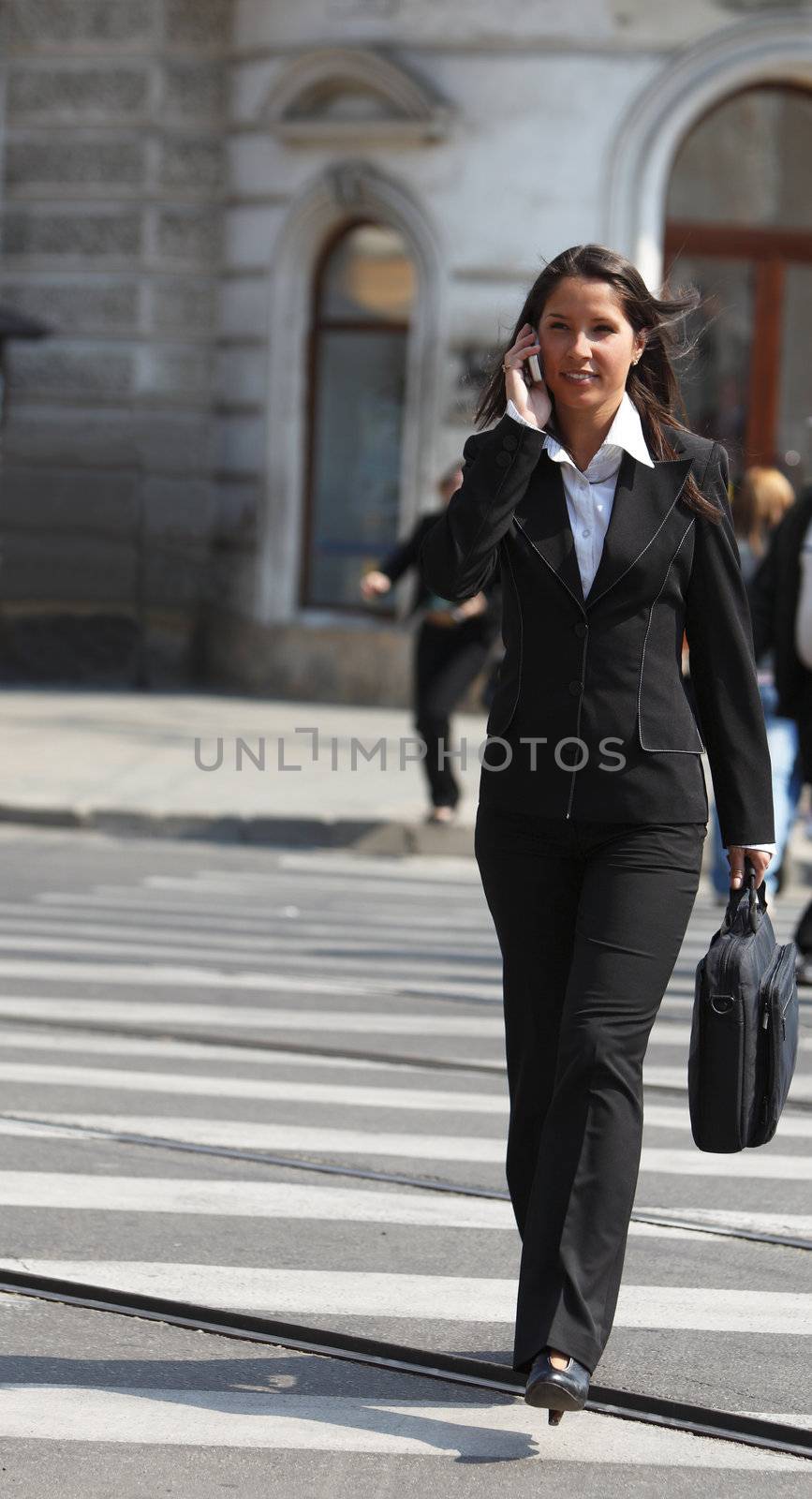 Young businesswoman on the phone crossing the street in a city.