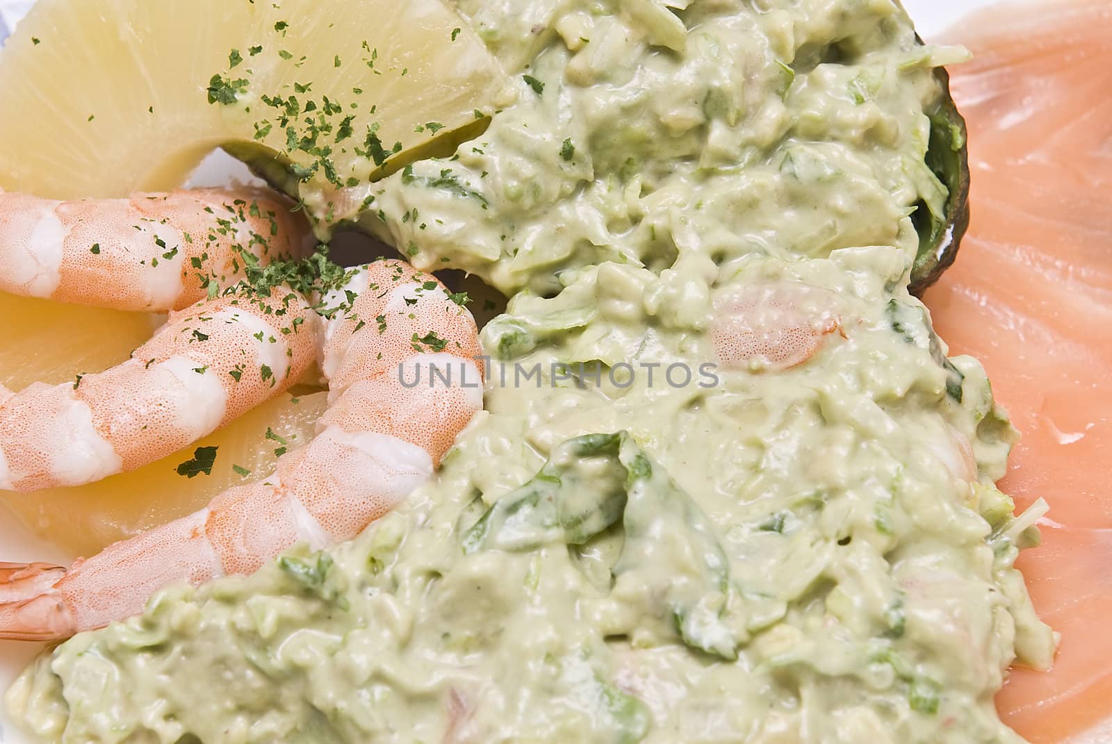 Avocado salad decorated with prawns, a slice of pineapple and a slice of salmon.