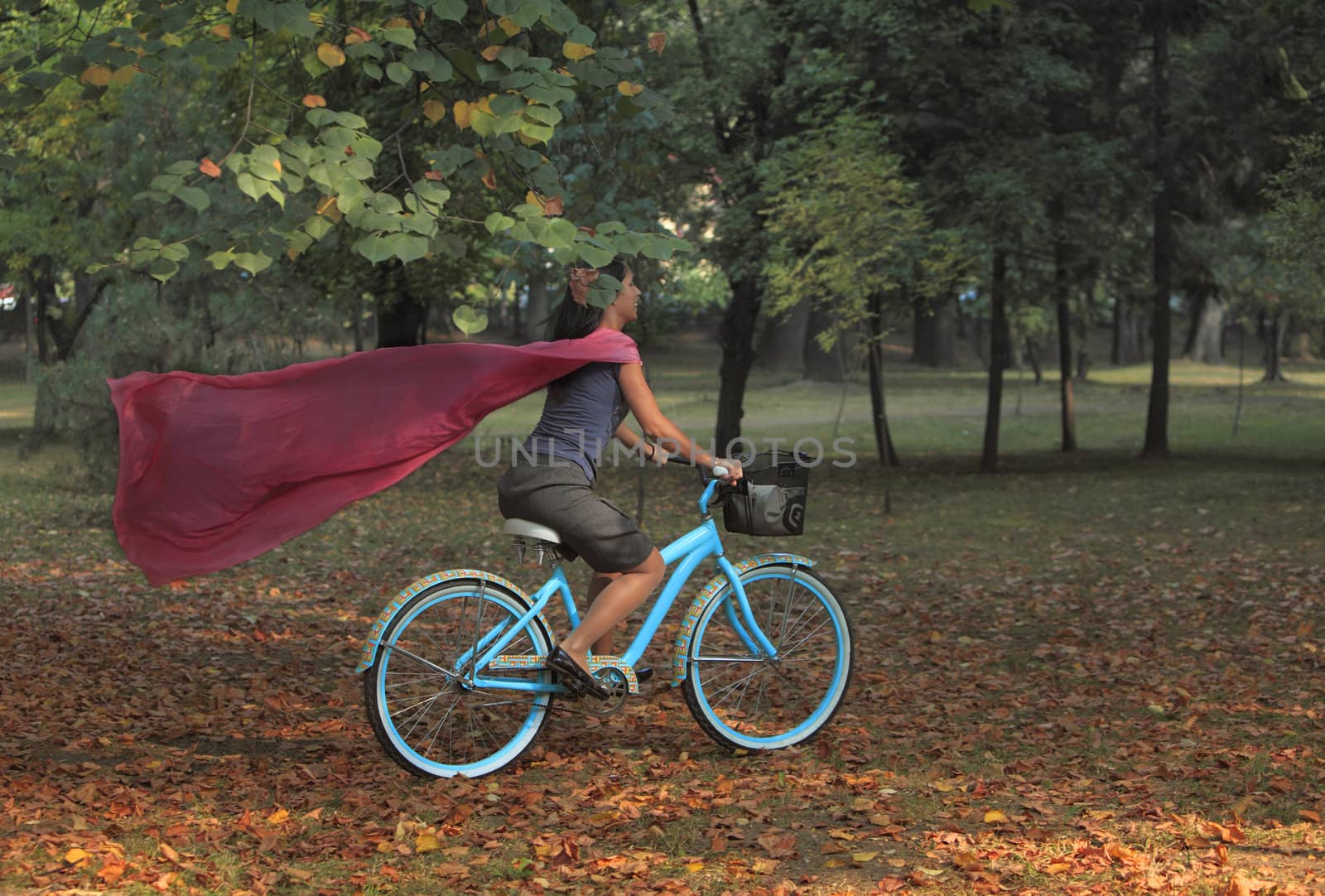 Image of a happy young woman with a pink scarf riding a bicycle in an early autumn park. 