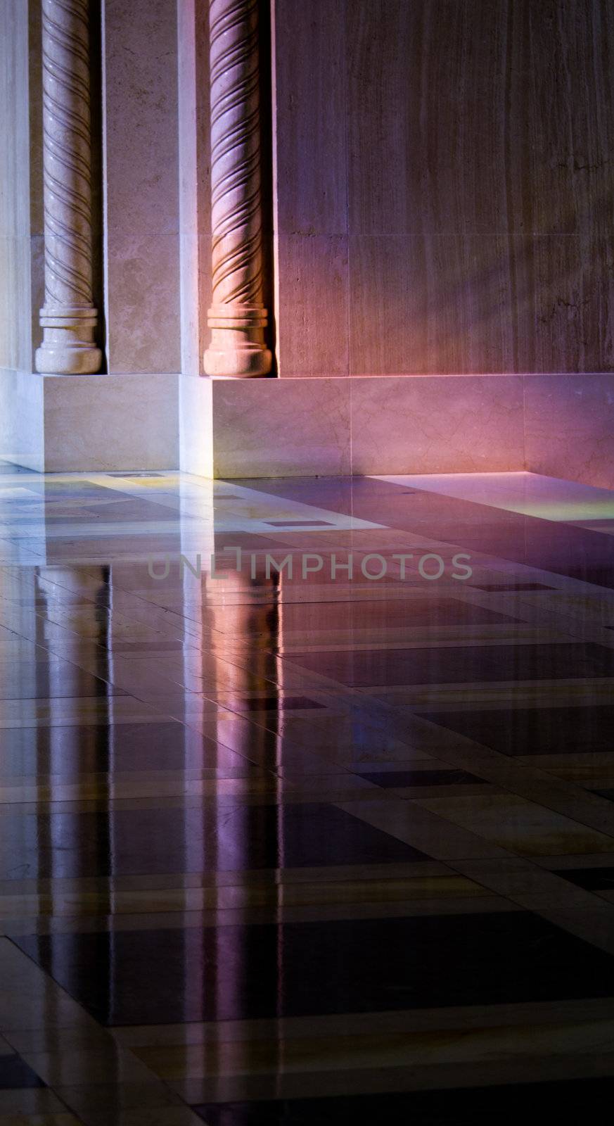 Colorful light from a stained glass window in a cathedral falls on the polished marble of the church illuminating the carved pillars and reflecting in floor