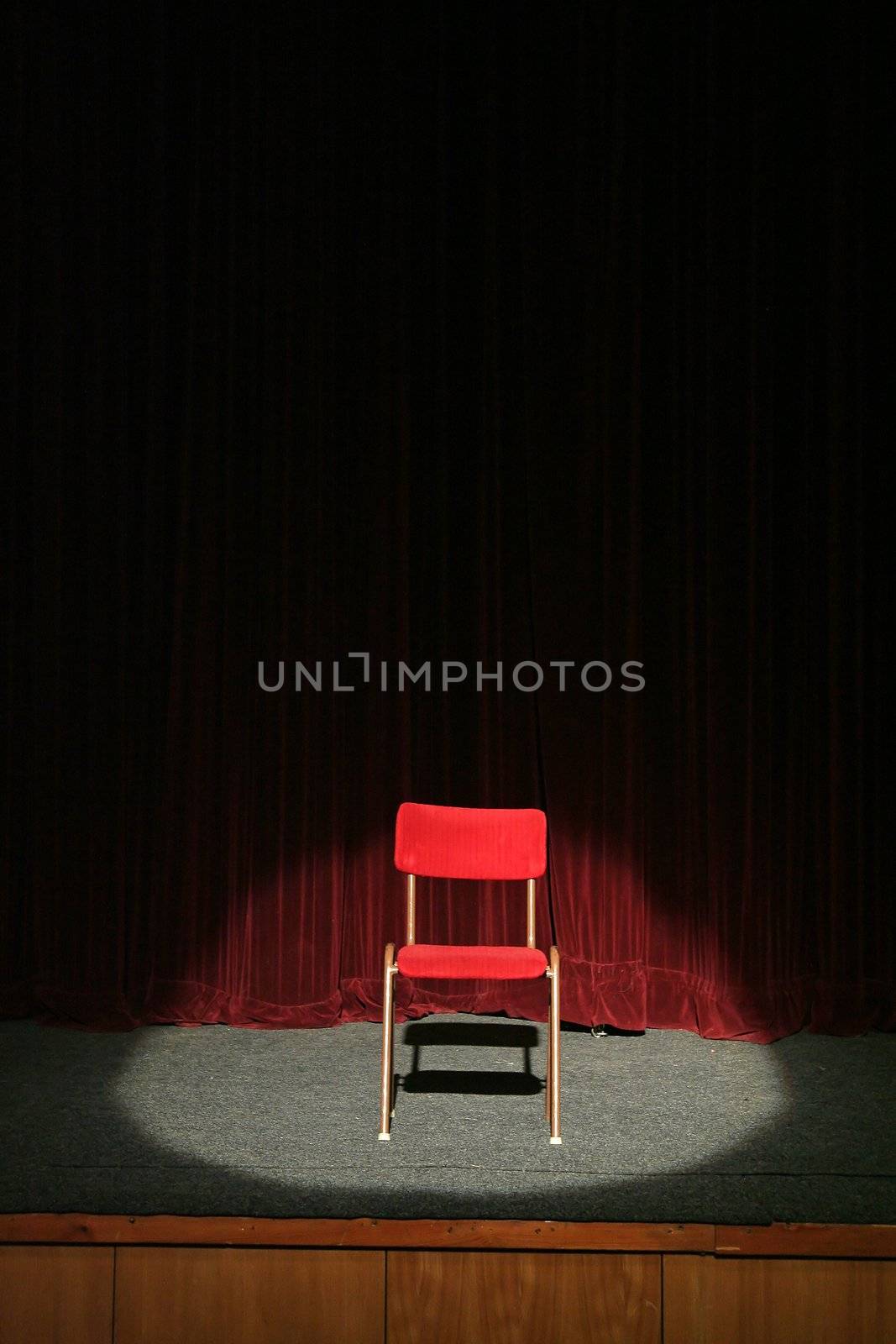 red chair on theatre stage lighted with spotlight, red curtain in background