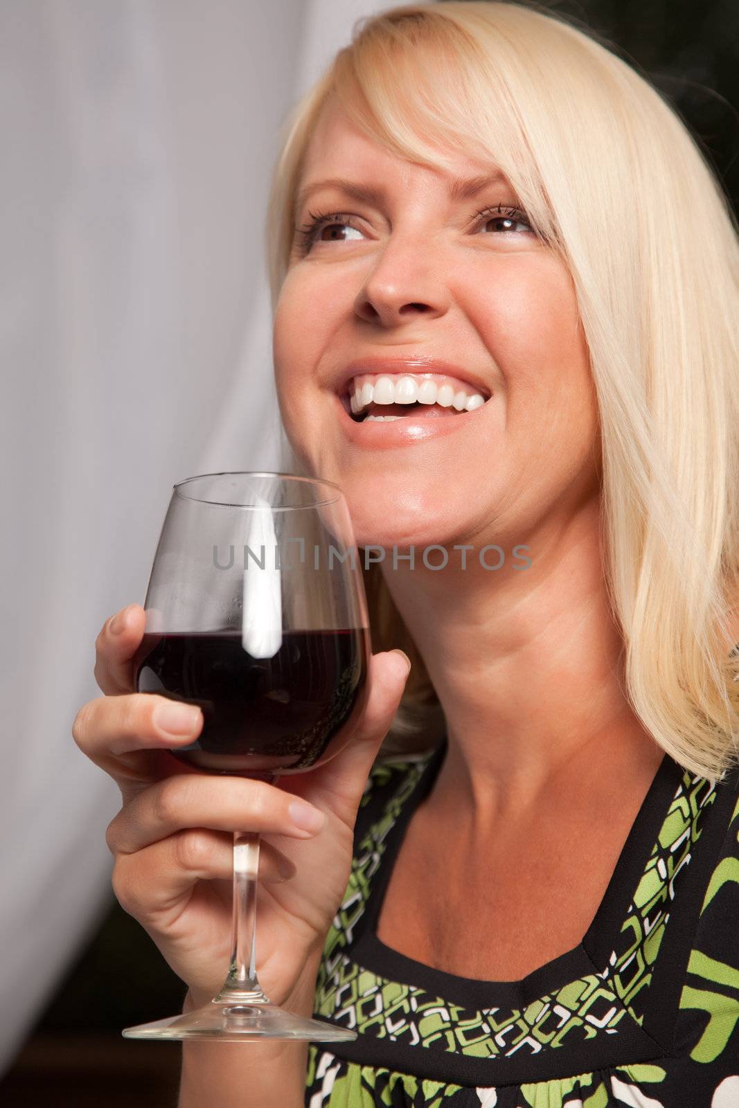 Beautiful blonde smiling woman at an evening social gathering tasting wine.