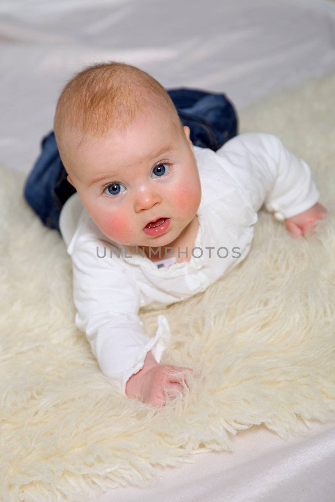a baby with blue eyes on the belly and looks up into the direction of the camera

