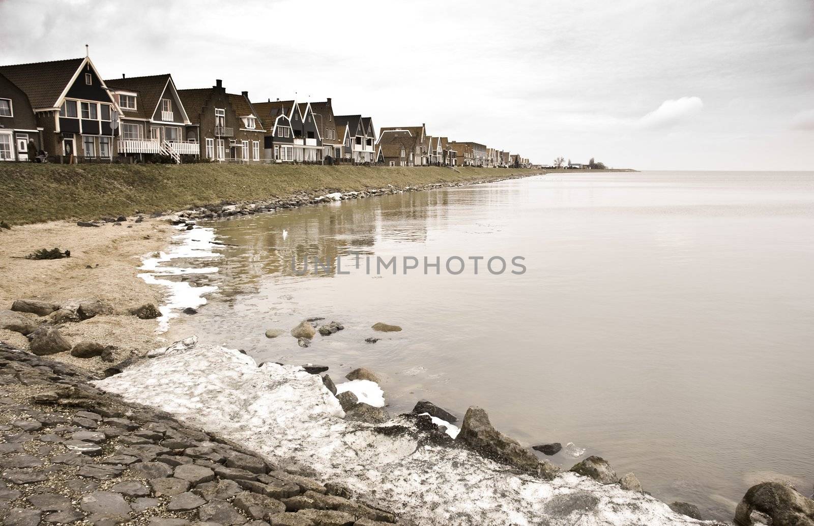 Old Dutch fishing village on dark and cloudy, rainy day in winter with snow and some melting ice at the lake. Image with old age colors. 