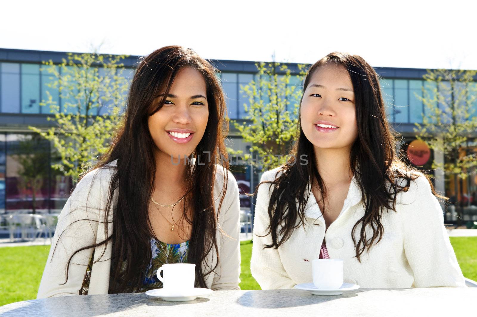 Two girl friends sitting and having drinks at outdoor mall