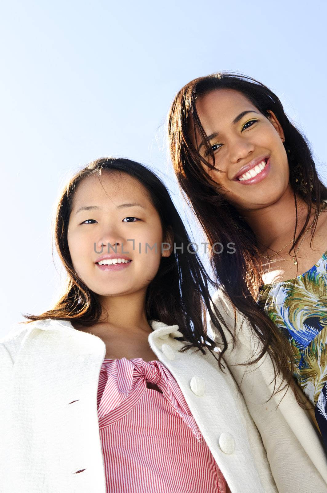 Two diverse young girlfriends smiling into camera