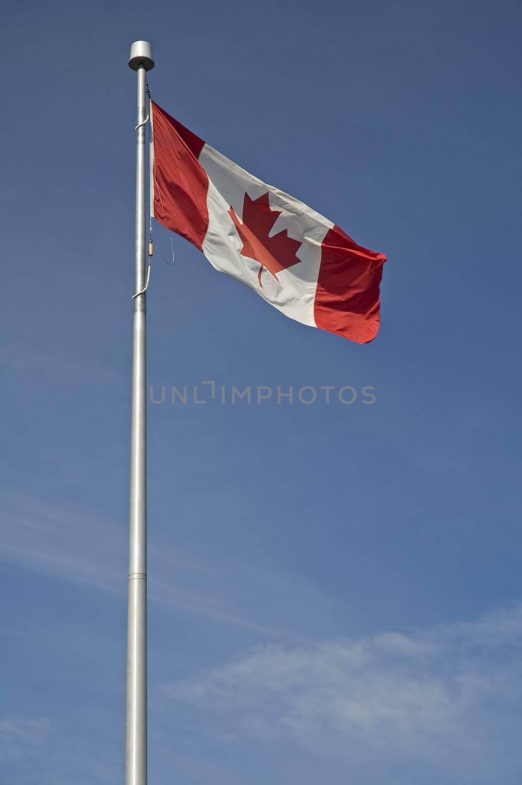 waving canadian flag on steel post, blue almost cloudless sky