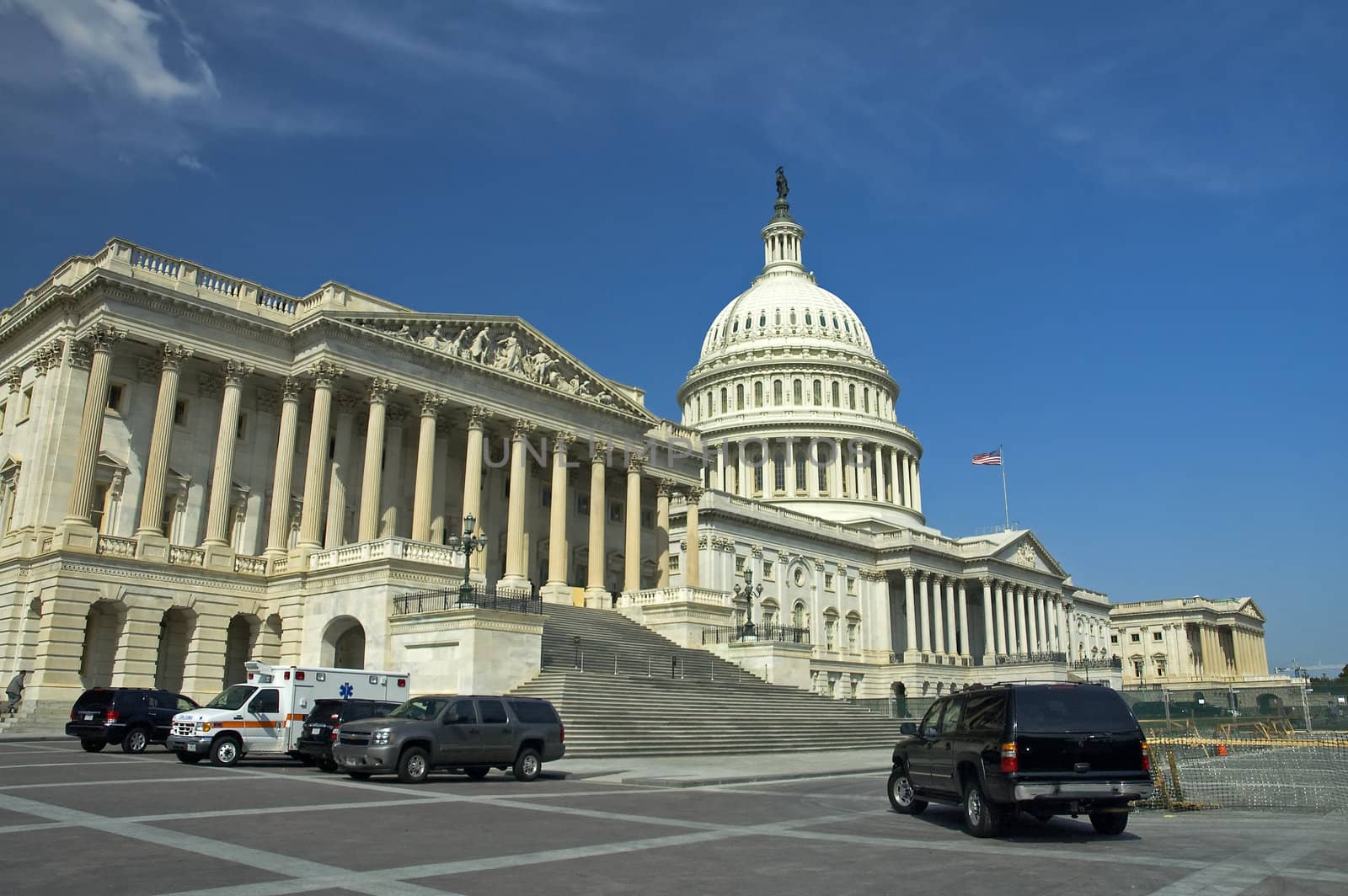 The Capitol in Washington, D.C. Security cars and ambulance in foreground, waving american flag