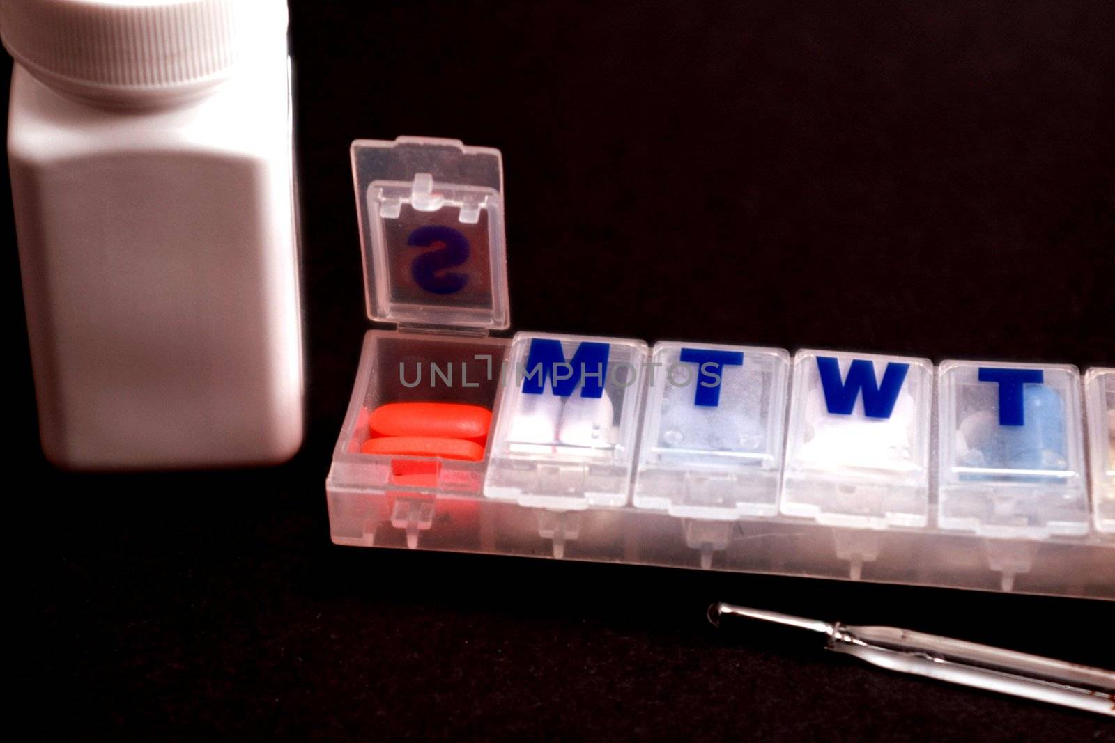 Open pill box, thermometer and medicine bottle on black background.