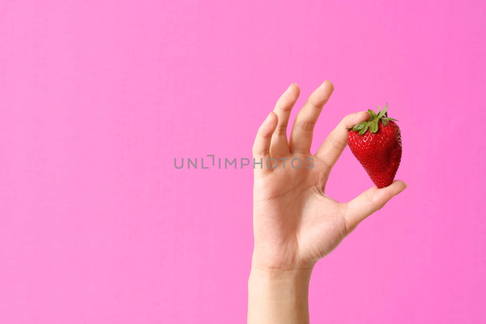 A woman holding a strawberry against pink background
