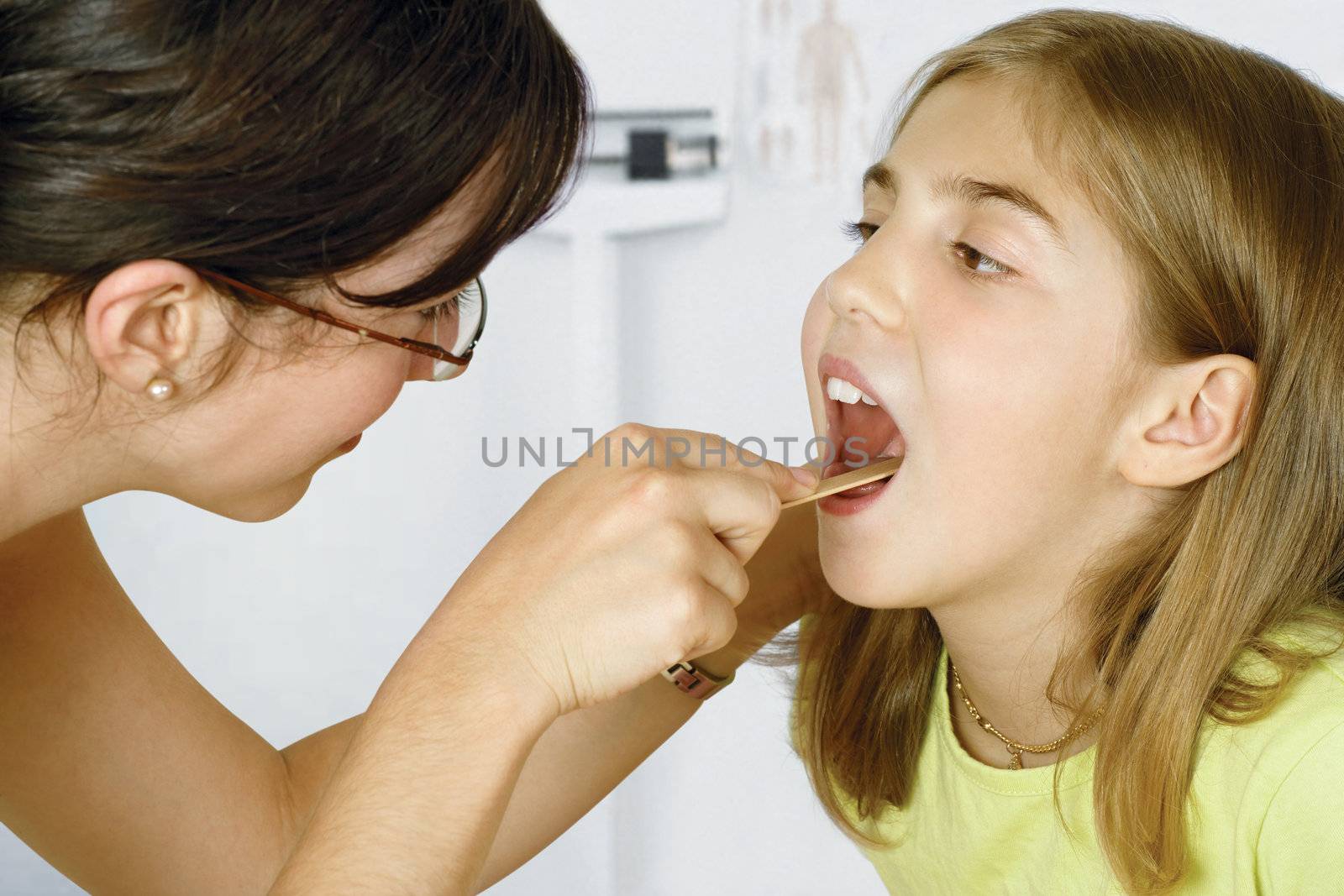 Doctor in her office checking the throat of a young patient.
