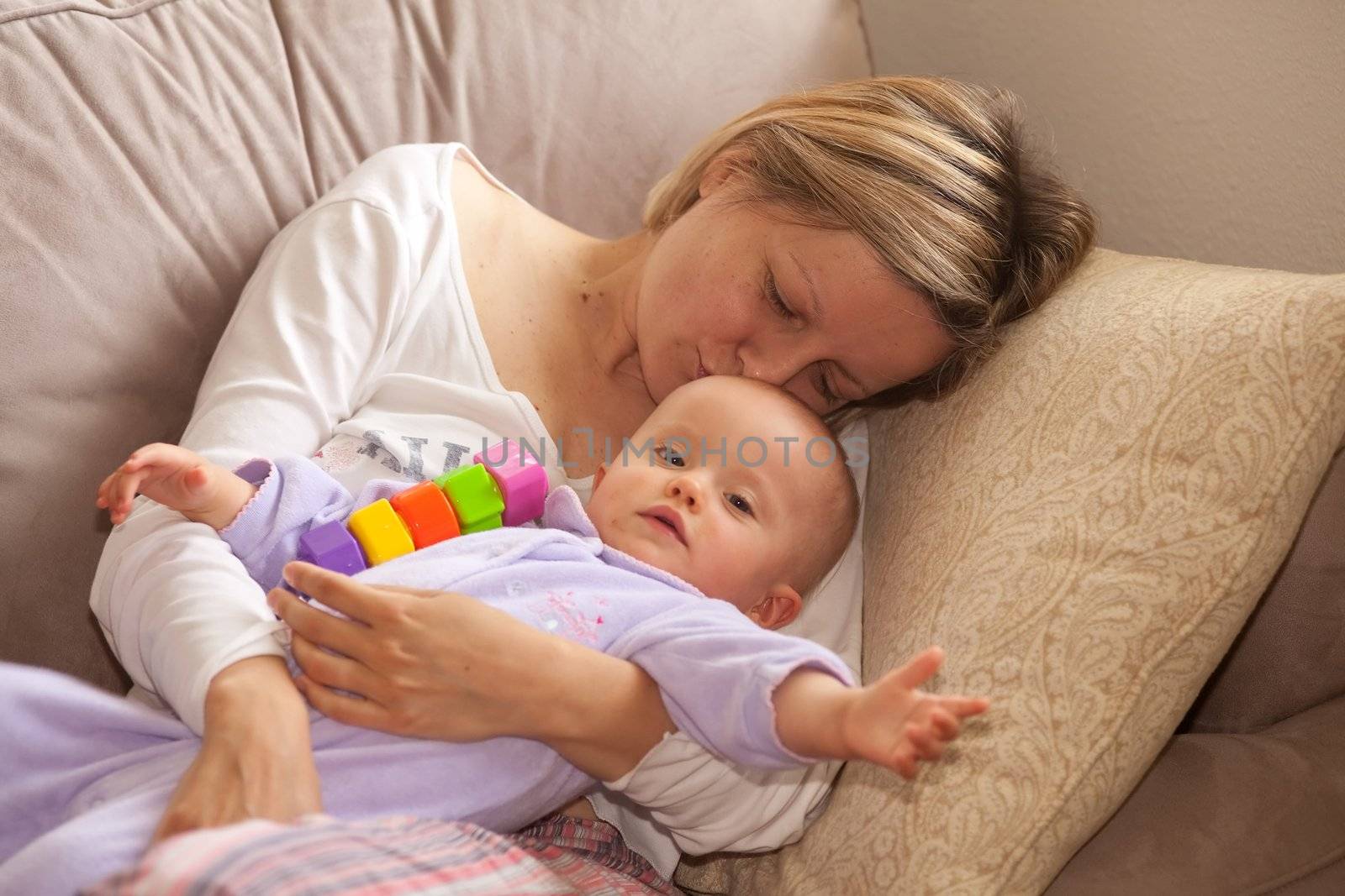 Happy beautiful laughing mother lies on the sofa with her baby.