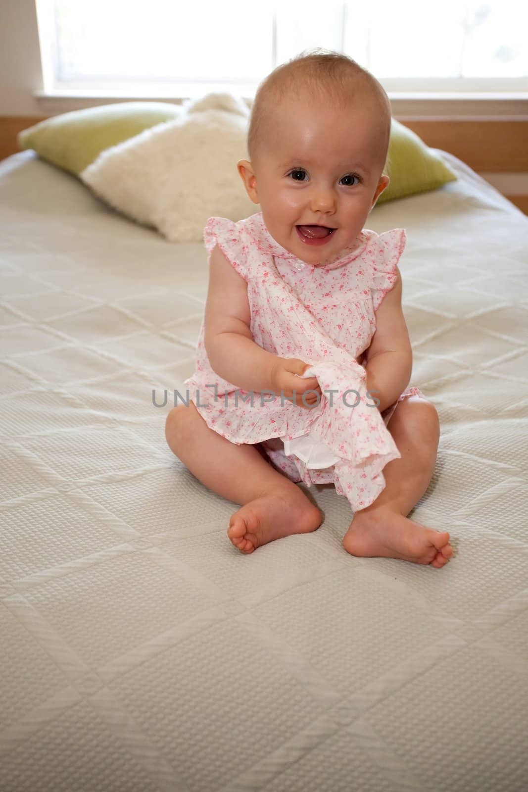 Cute little caucasian baby girl wearing pink dress and sitting on a bed.