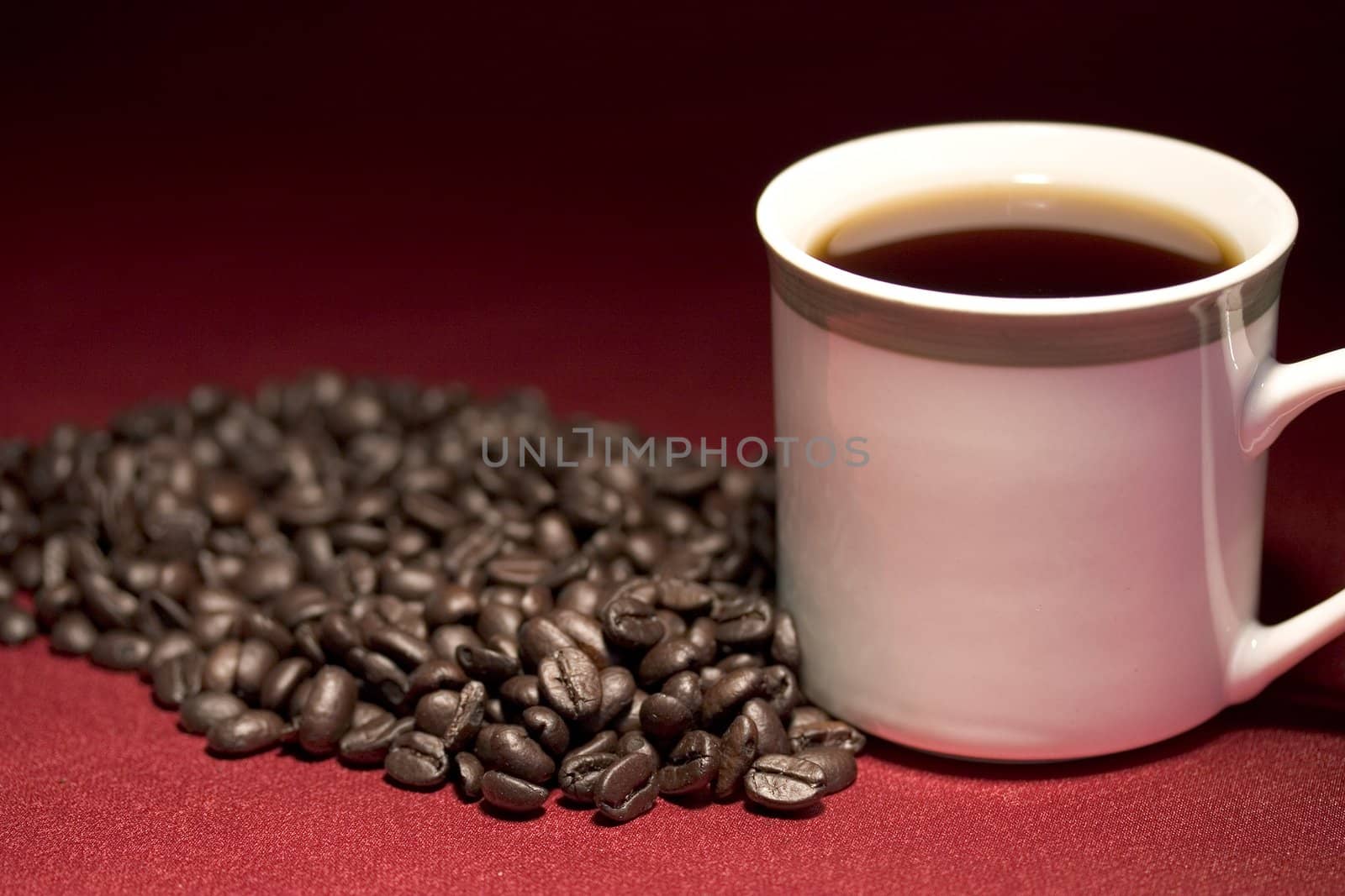 White coffee cup and beans sitting on a red background fade to black
