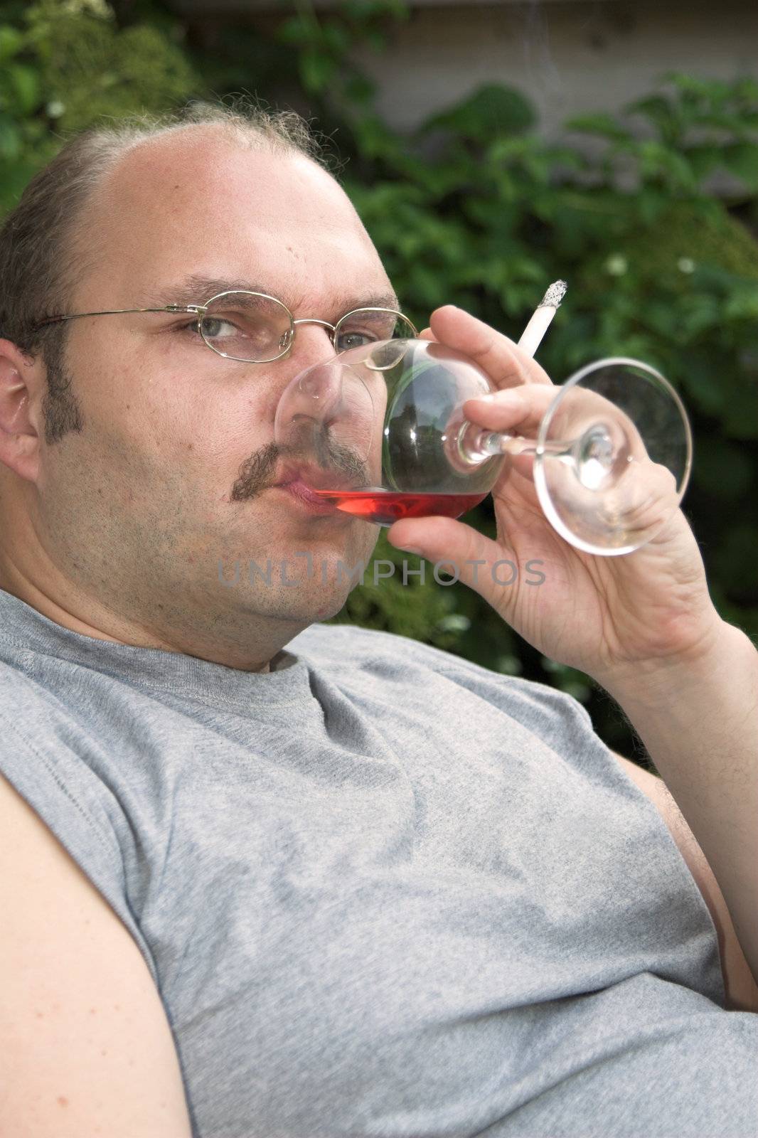 Overweight mature man sitting in a chair drinking too much and smoking too much
