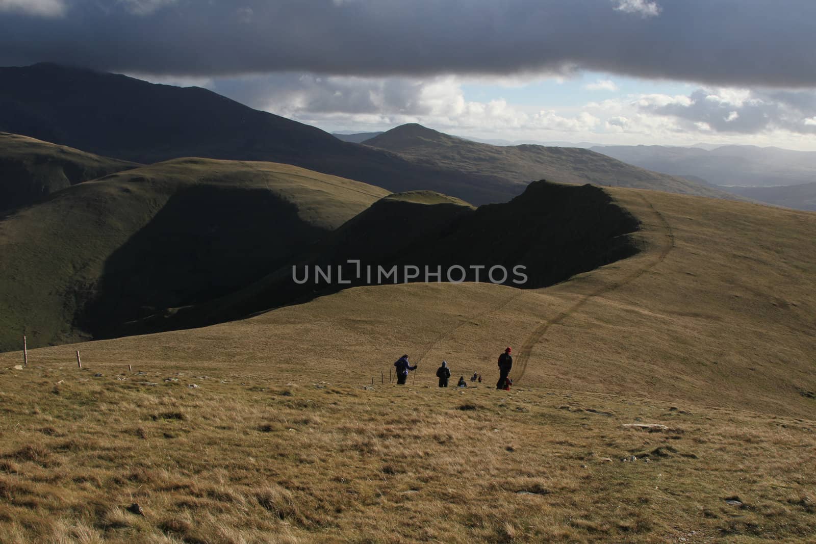 Hill walkers enjoying the great outdoors on a grassy mountainside  with blue sky and cloud.