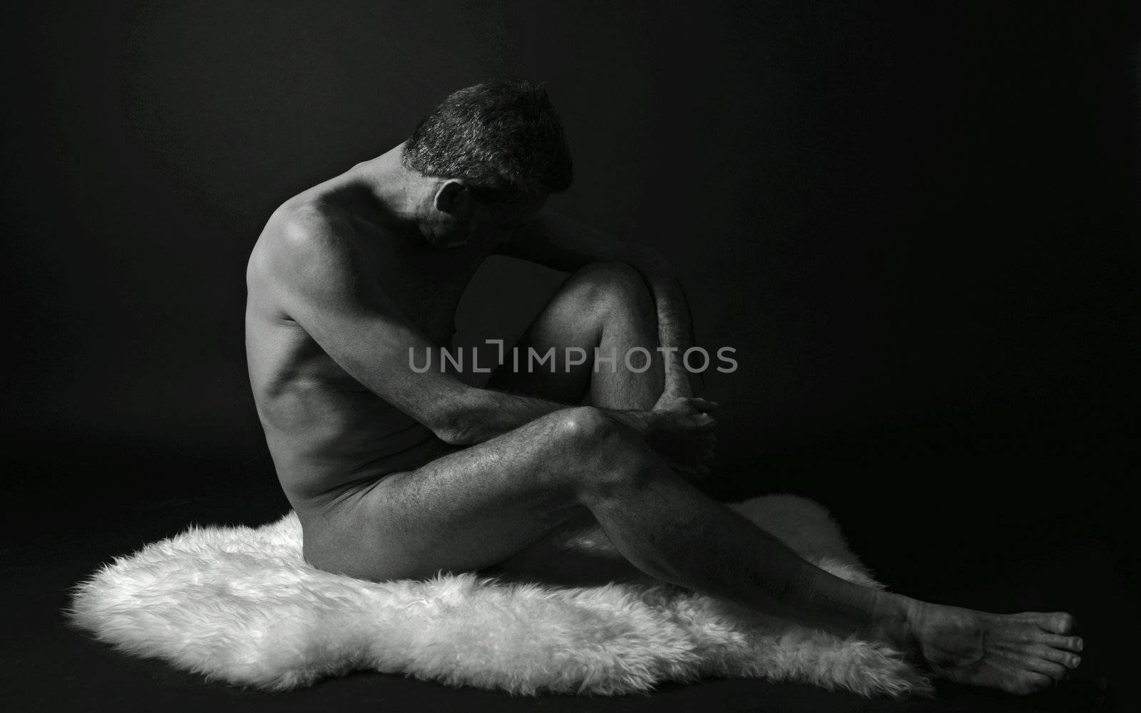 nude man sitting in front of black background